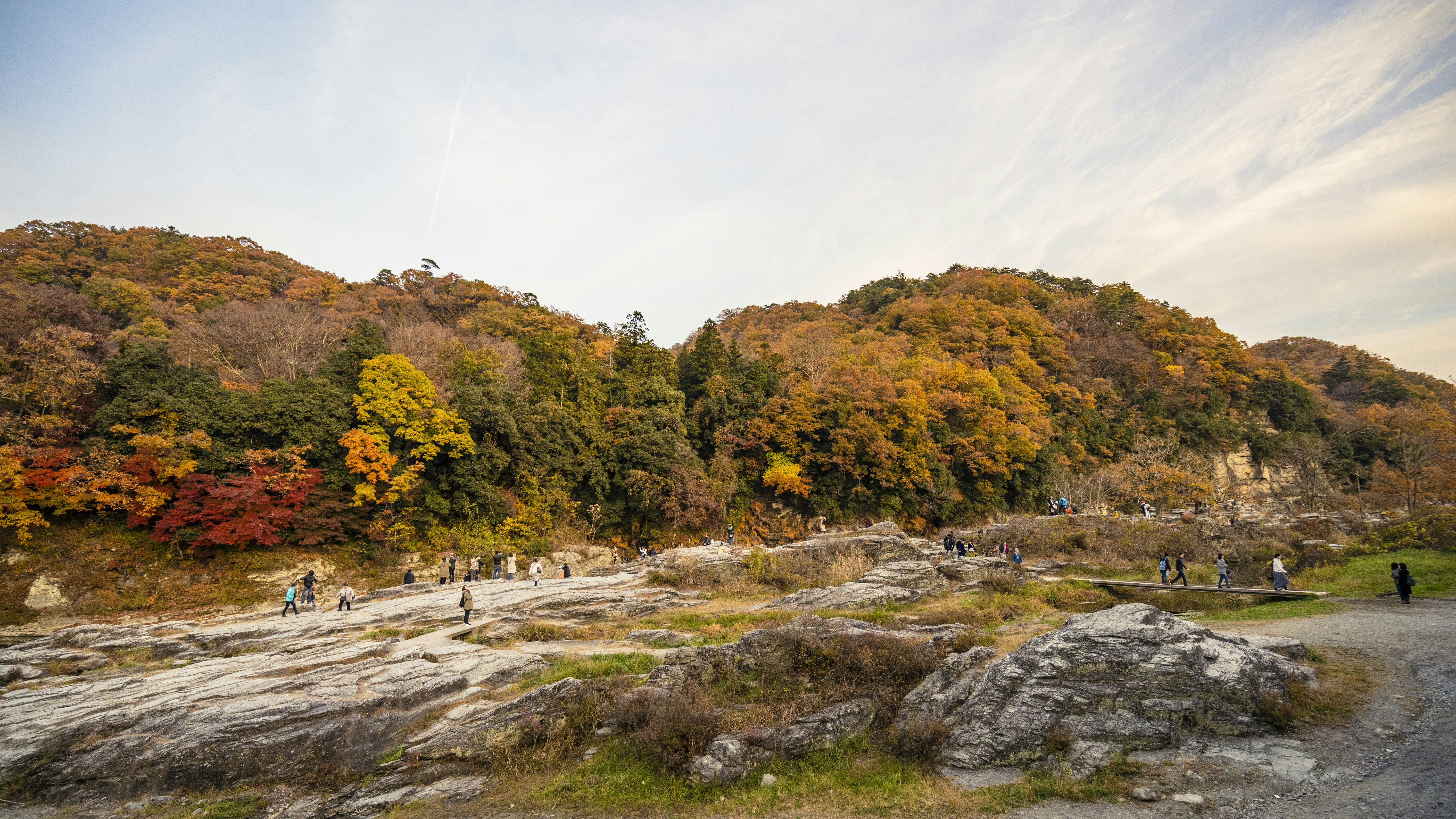People hiking across rocky terrain with a backdrop of autumnal foliage