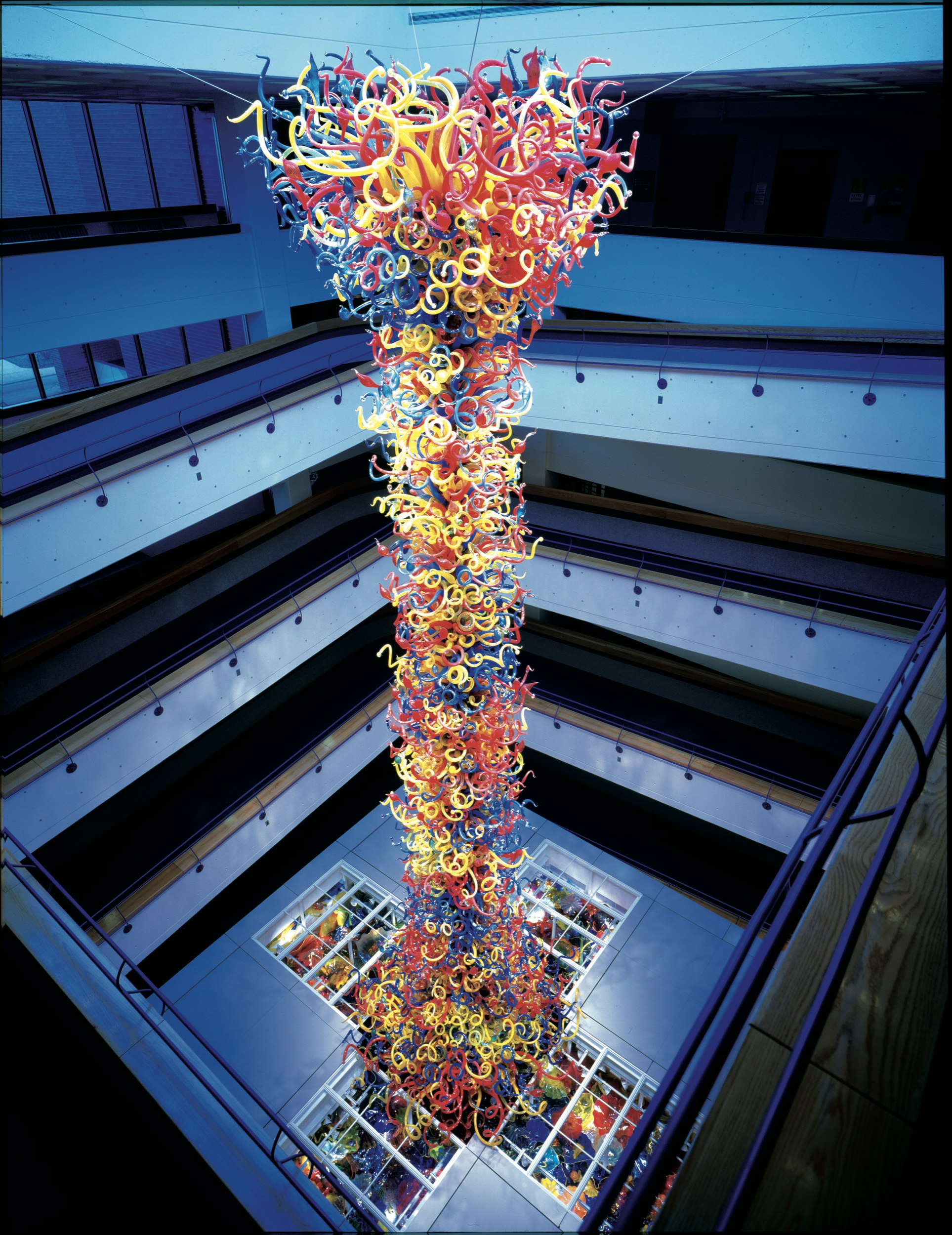 A riot of red, yellow and blue curlicues made of glass are stacked into a tall tower and illuminated, visible from several layers of balconies on all sides; Where to see Chihuly in America