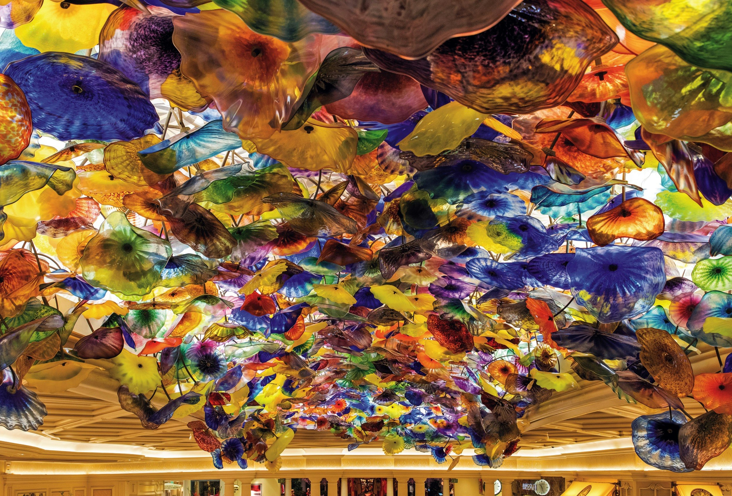 Red, yellow, orange and blue glass flowers are suspended from an illuminated ceiling in a casino; Where to see Chihuly in the USA