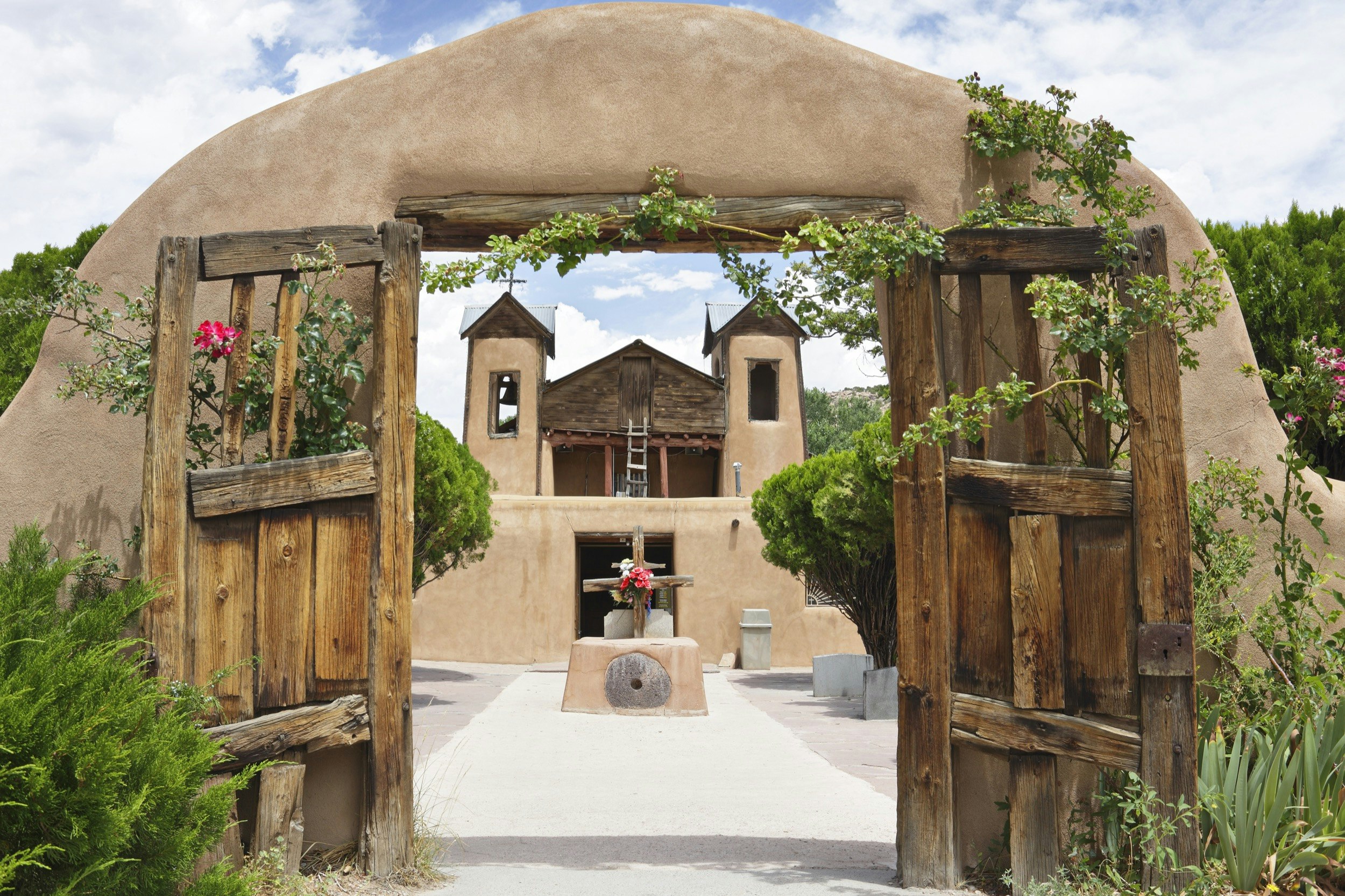 An old spanish chapel with an adobe and wood gate is seen on the High Road to Taos