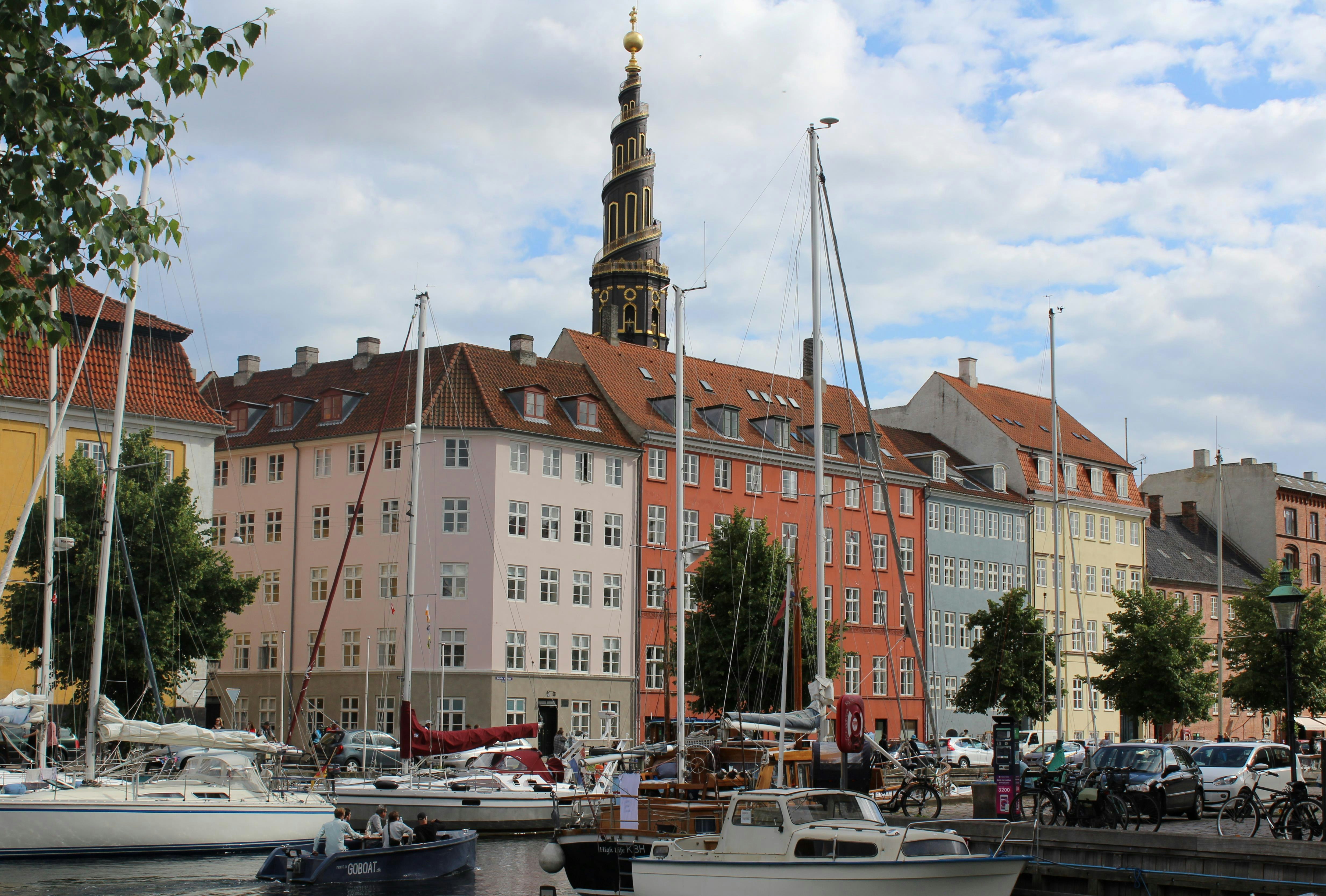 Many boats line the canals at Christianshavn in Copenhagen; the large buildings along the water's edge are painted in pastel colours.