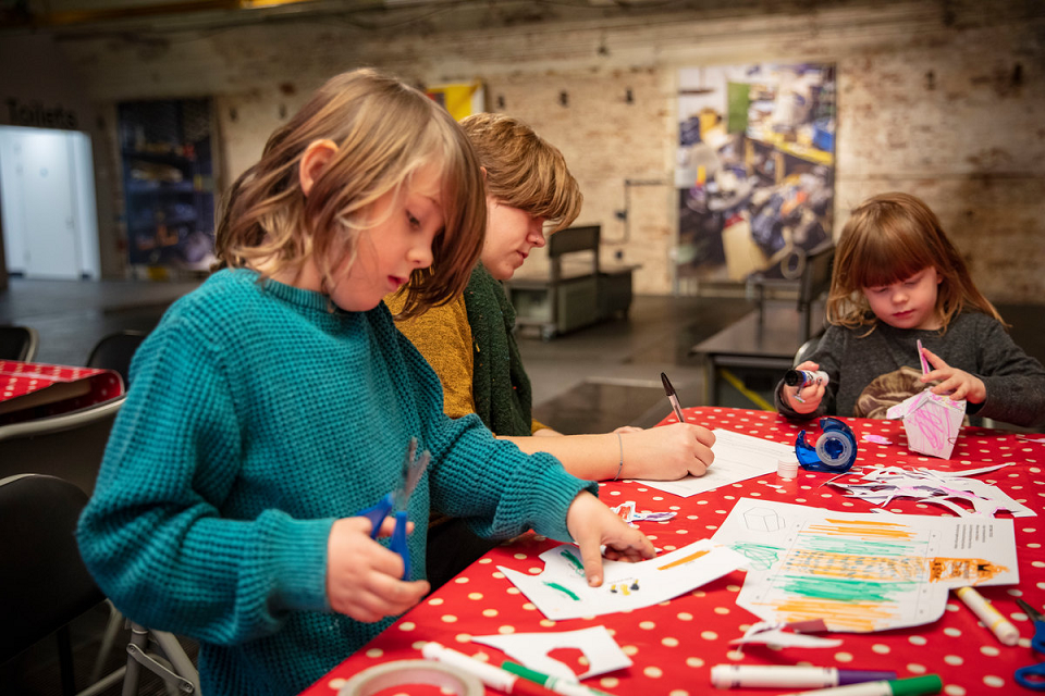 Three children sit at a table with a polka-dot table cloth doing arts and crafts in London's Postal Museum