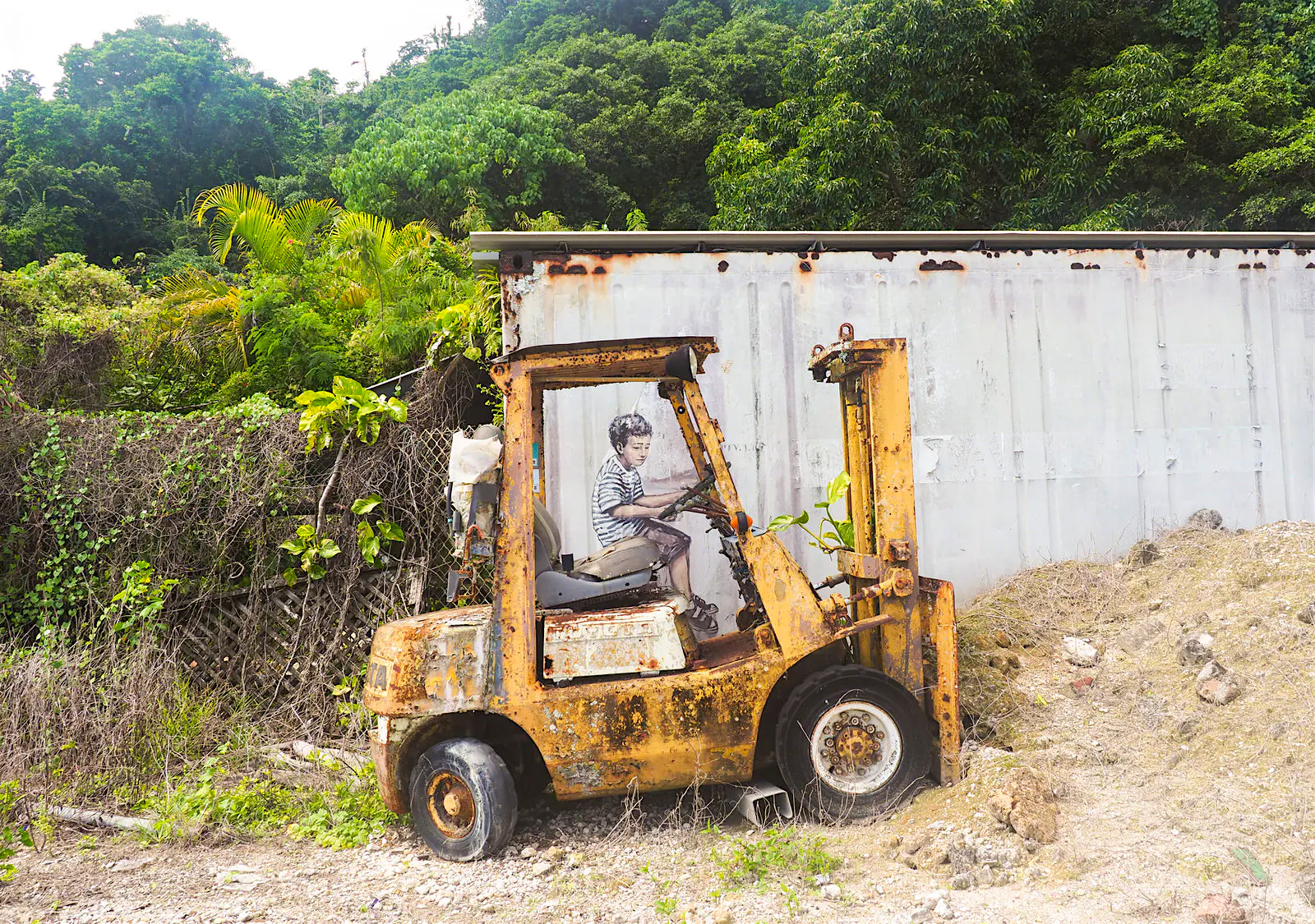 Christmas Island has a fledgling street art scene. Image credit Sarah Reid.jpg A forlorn forklift is parked next to an old shipping container; an image of a boy has been painted on the container to look as if he is driving the forklift