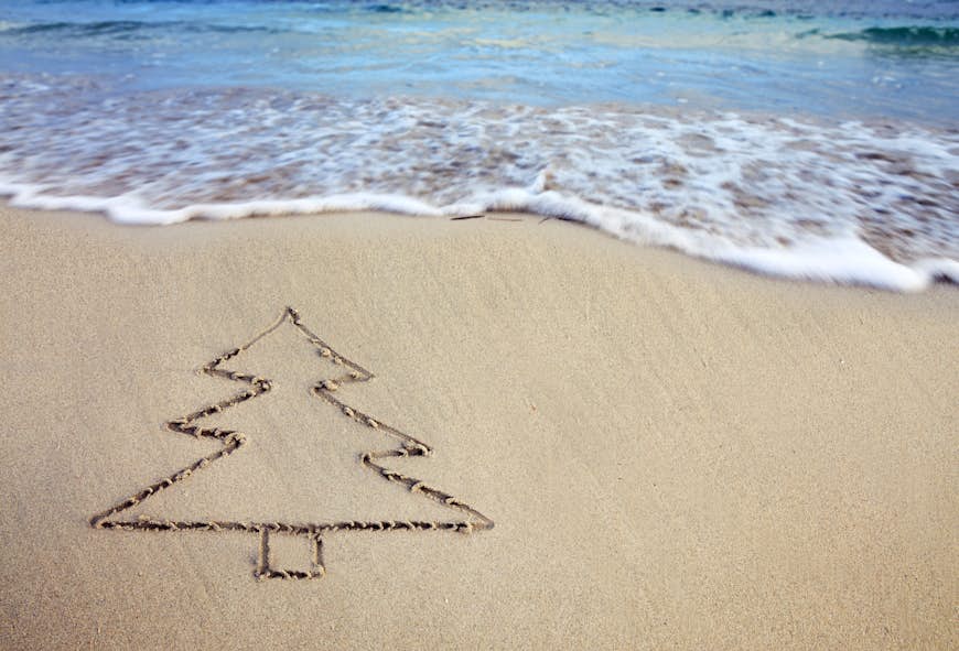 A drawing of a Christmas tree is etched in the sand next to a beach
