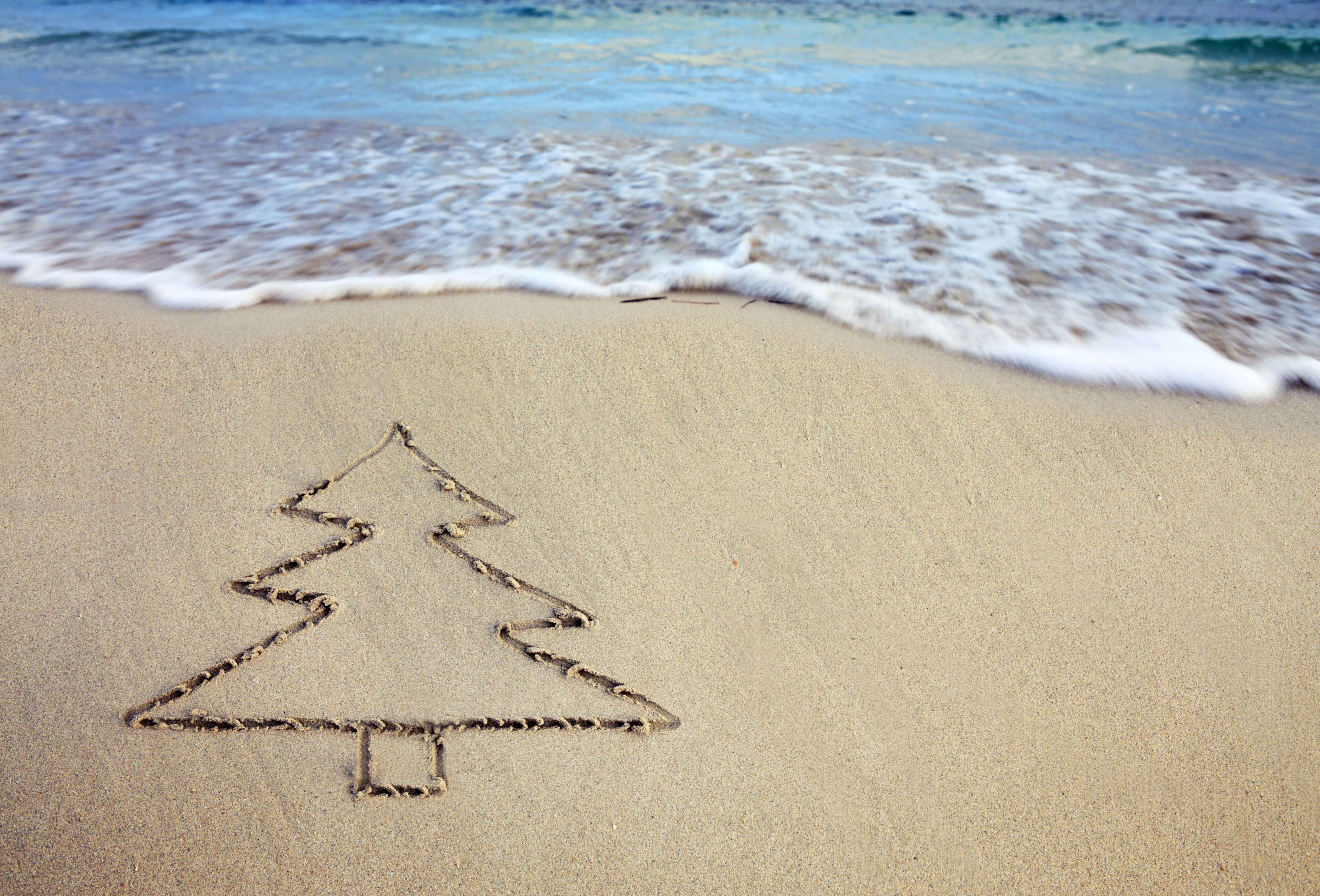 A drawing of a Christmas tree is etched in the sand next to a beach