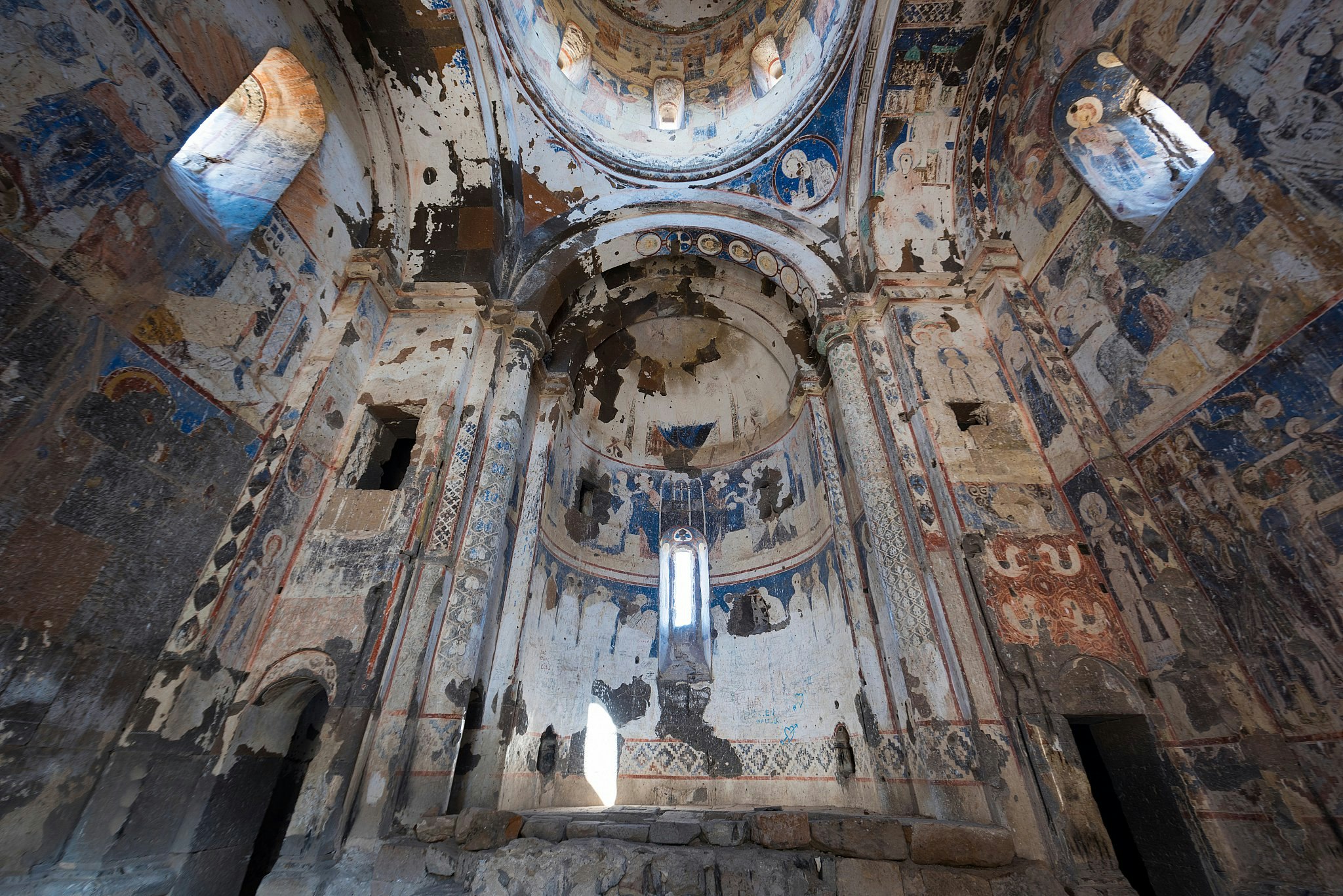 Colourful but faded and time-worn frescoes inside a domed church. 