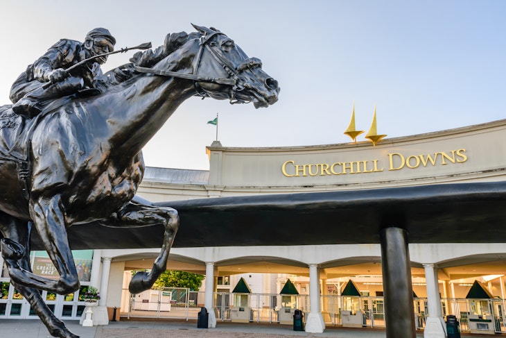 A statue of a jockey riding a horse sits outside the entrance to Churchill Downs.