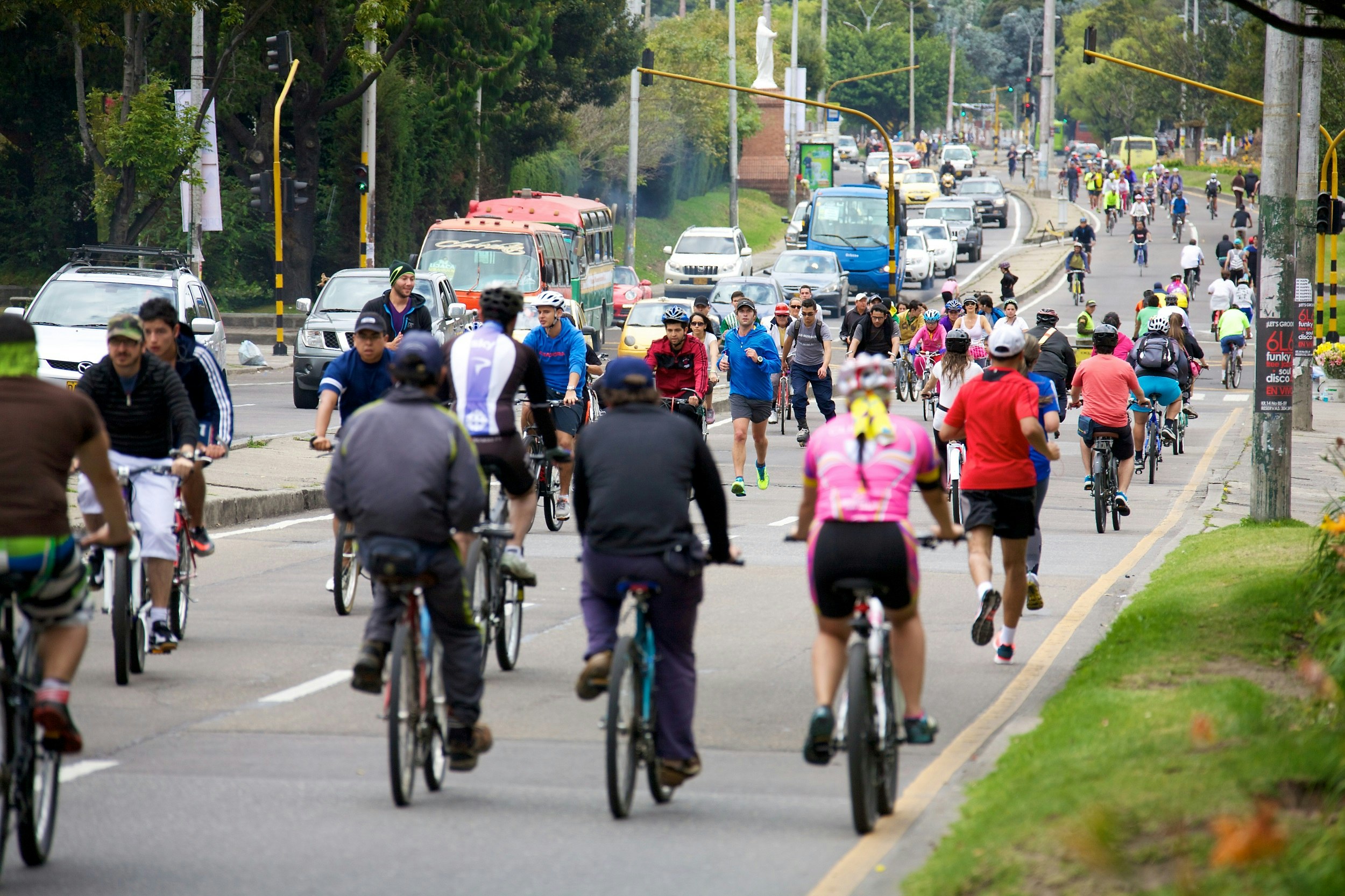 A view looking down a large street within Bogota; one side of the divided road is packed with cyclists, runners and roller bladers taking part in Ciclovía. The other side of the road has vehicle traffic.