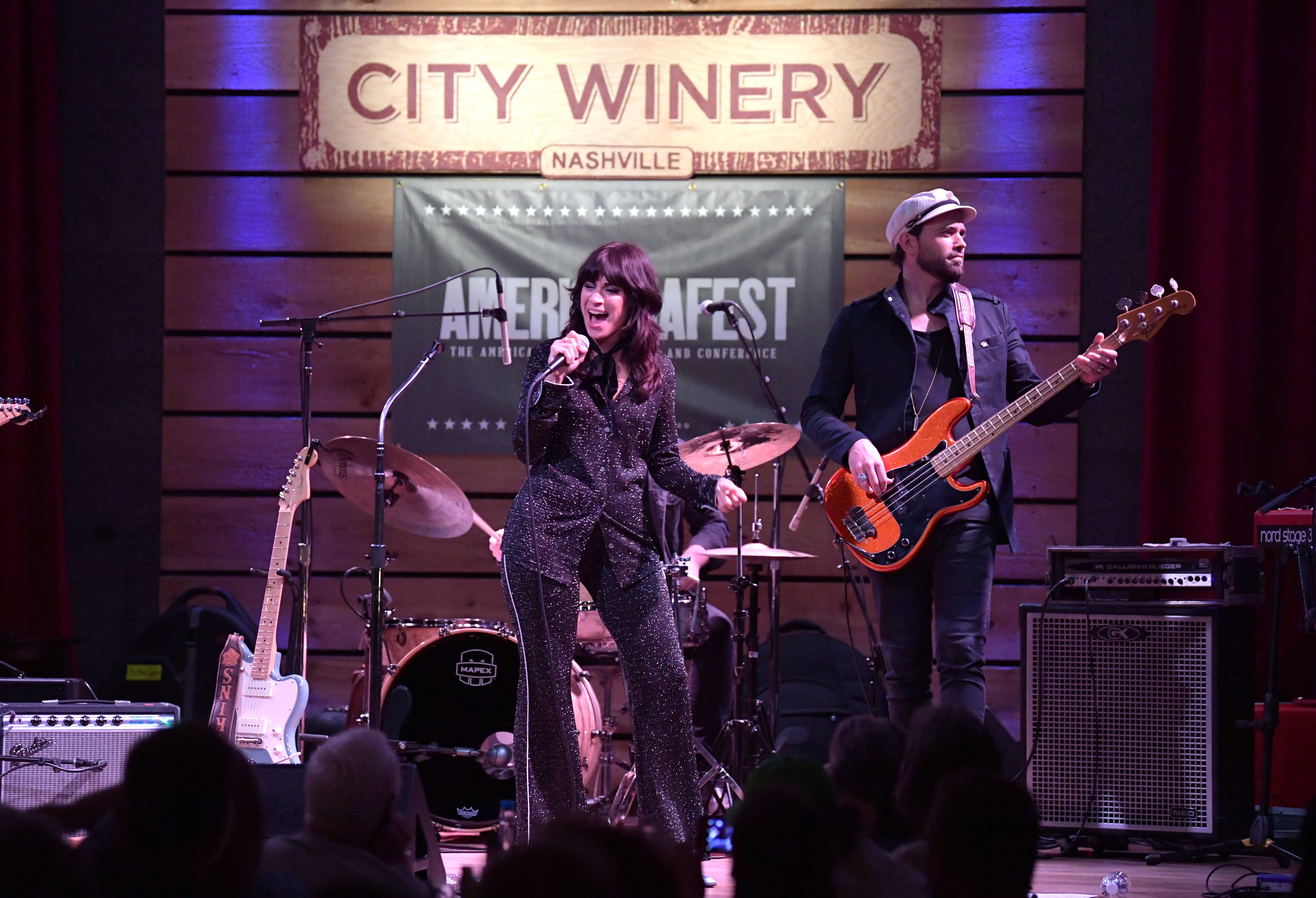 A woman wearing a sparkly suit sings into a microphone on a stage next to a man playing an orange guitar at City Winery in Nashville.