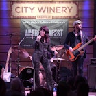 A woman wearing a sparkly suit sings into a microphone on a stage next to a man playing an orange guitar at City Winery in Nashville.