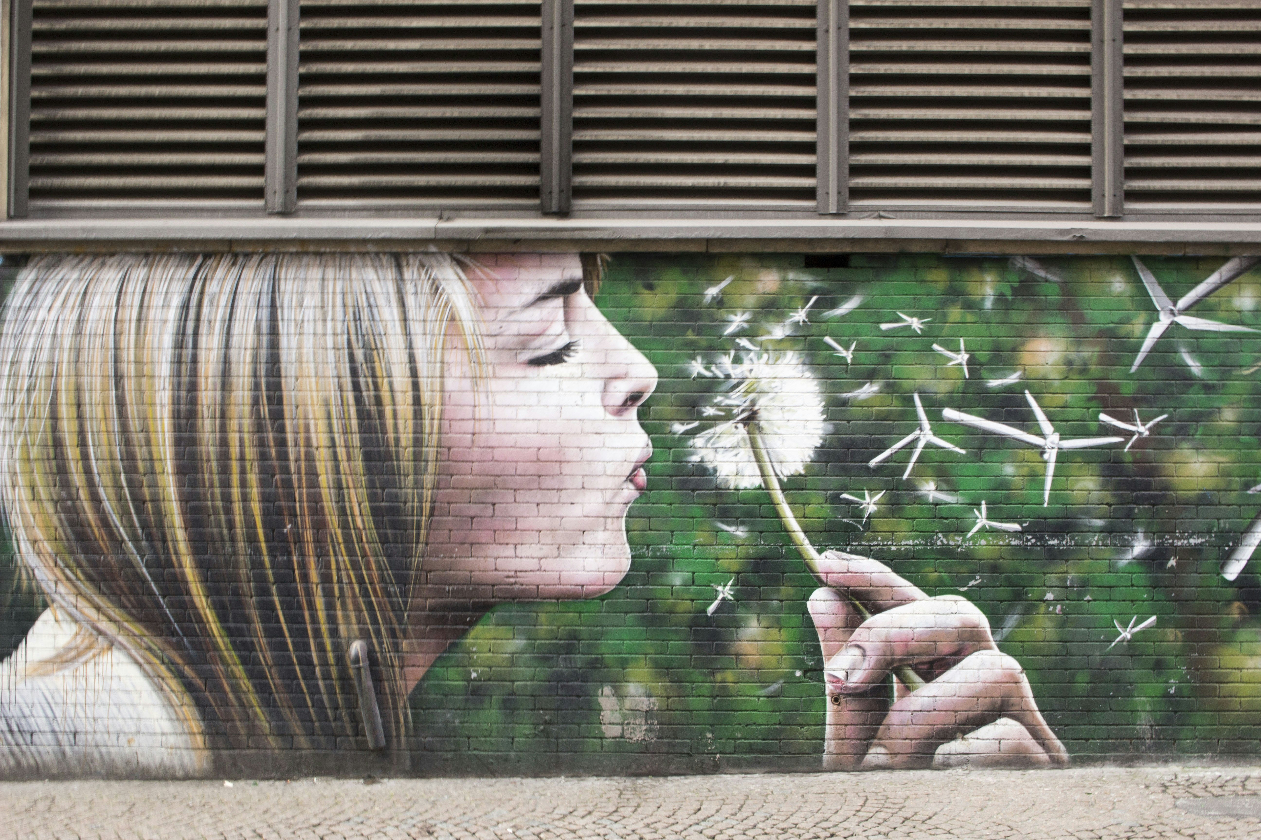 A mural of a blonde girl blowing a dandelion on a Glasgow wall.