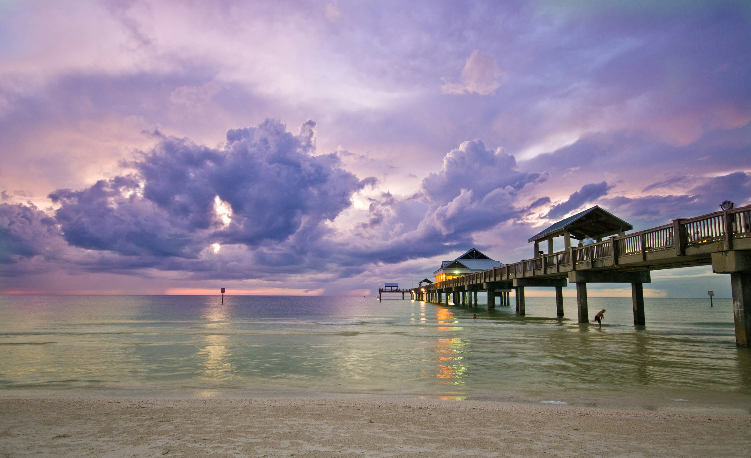 Purple clouds at sunset on a clearwater, white sand beach with the pier in view