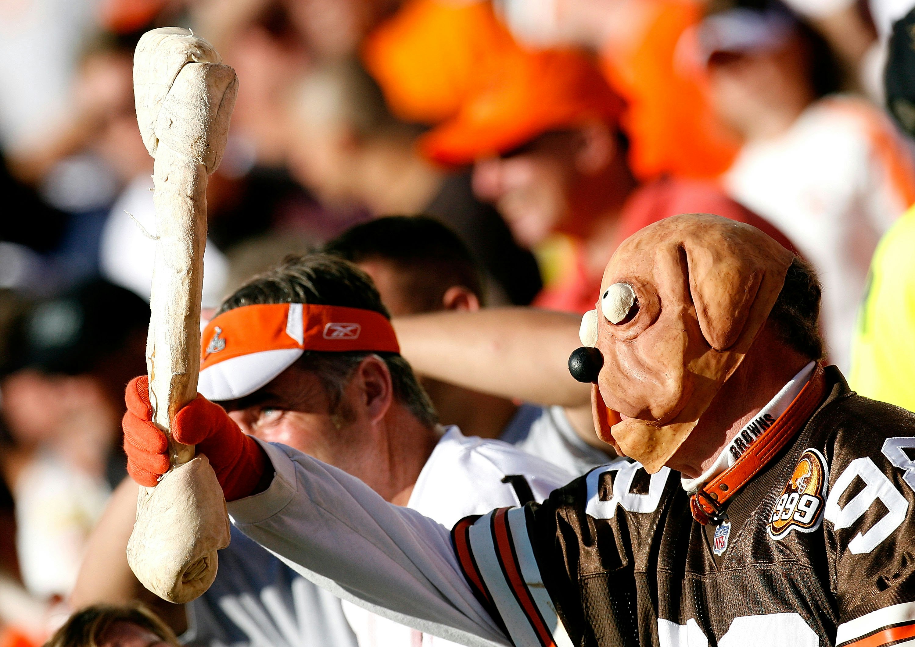 A man wears a dog mask and holds a giant dog bone during an NFL football game; nfl cities travel