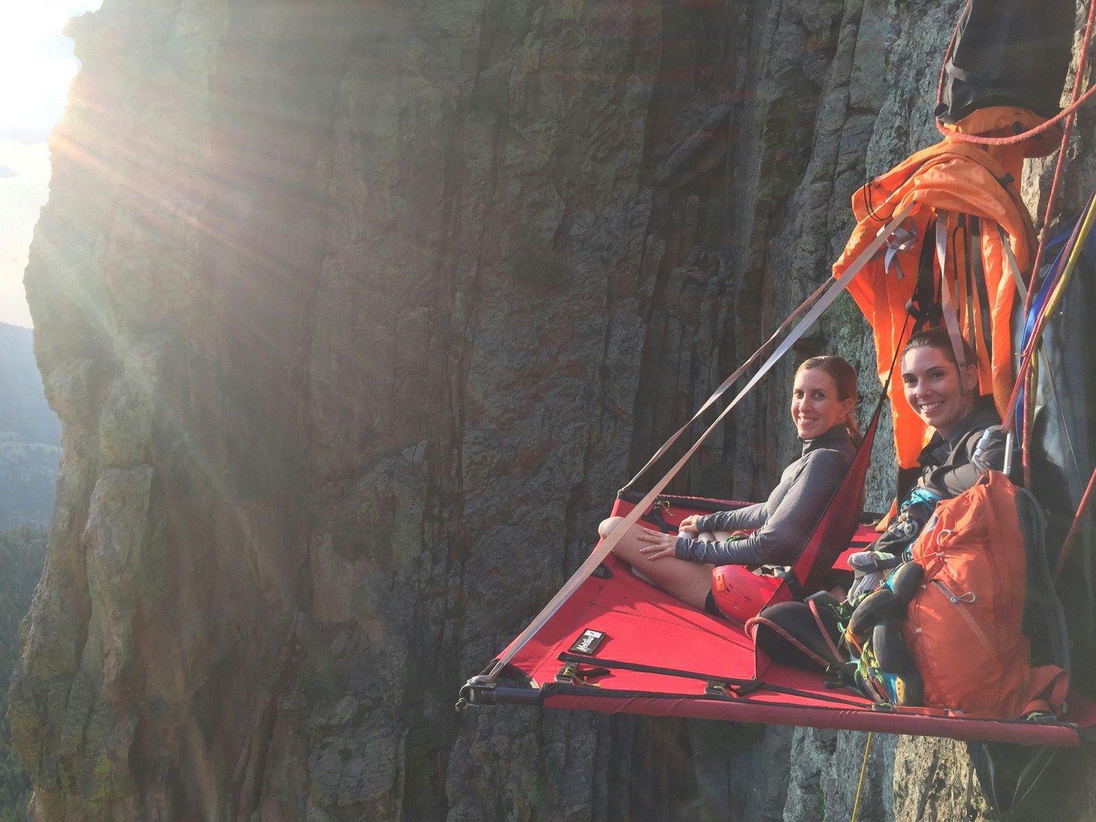 Two women sit on a hanging platform on the side of a cliff