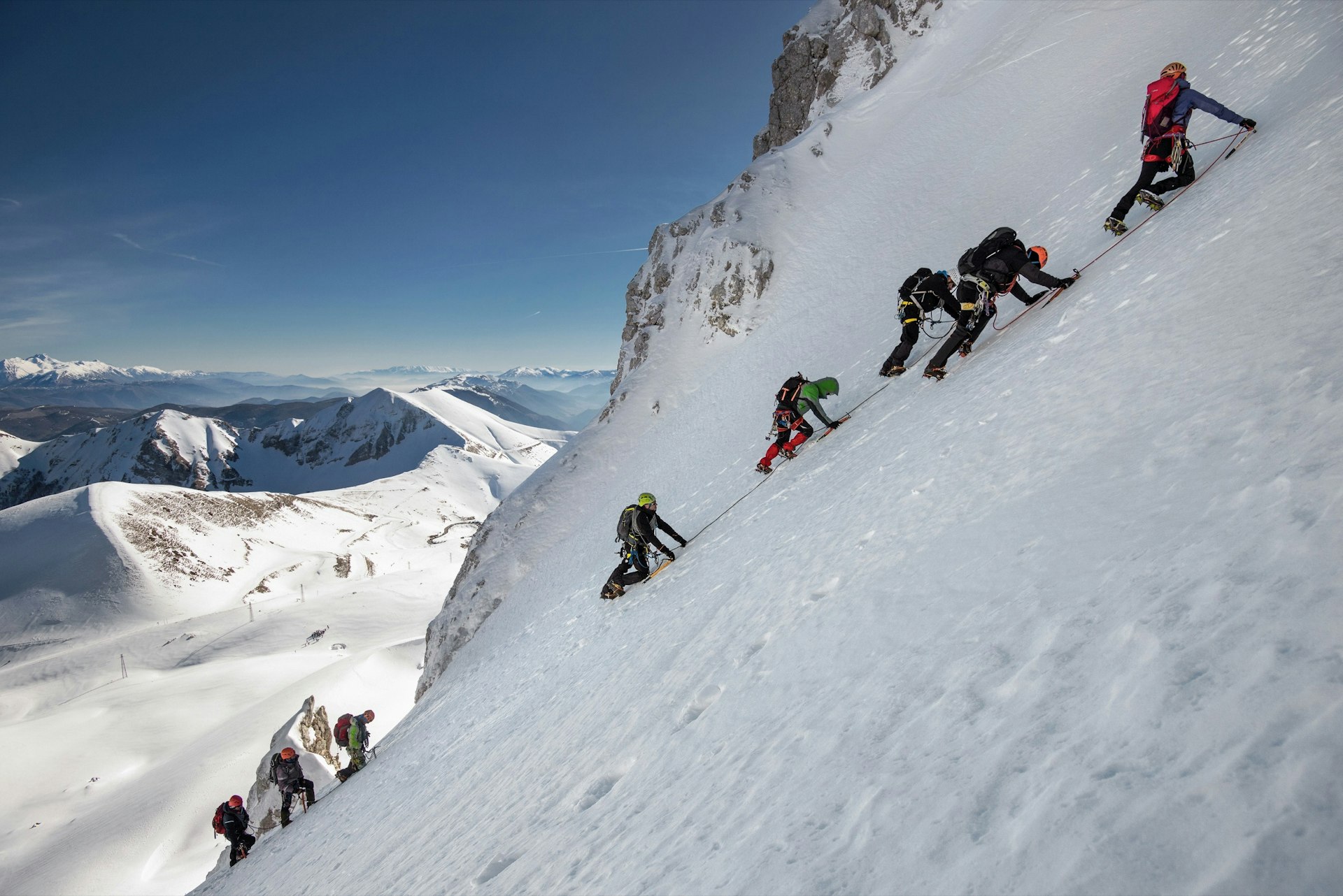A line of ice climbers ascends a steep snow-covered peak in France; Climbing fourteeners for beginners