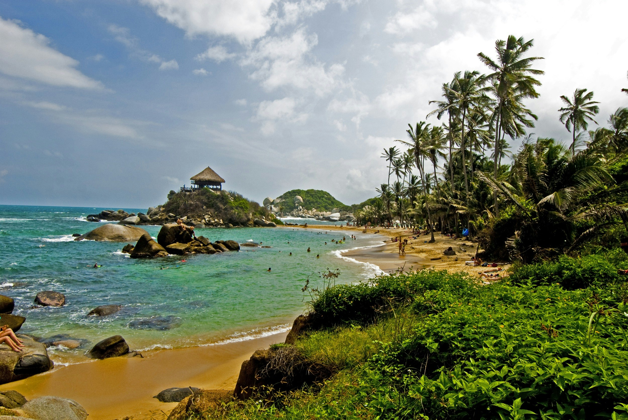 People party and play on a rocky beach cove in Colombia with crystal-clear blue green water and soft golden sand