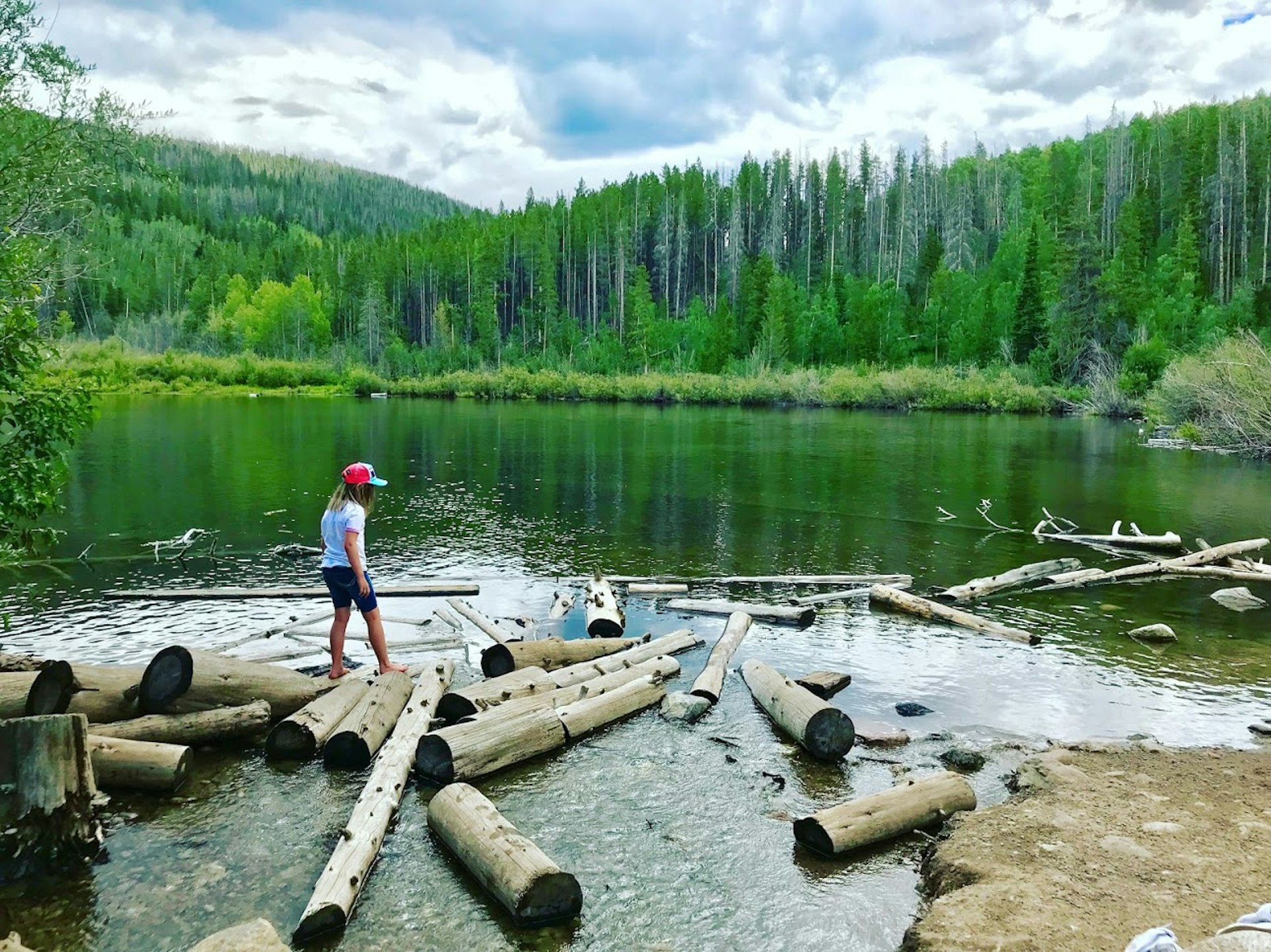A barefoot girl picks her way across logs in a high-alpine lake