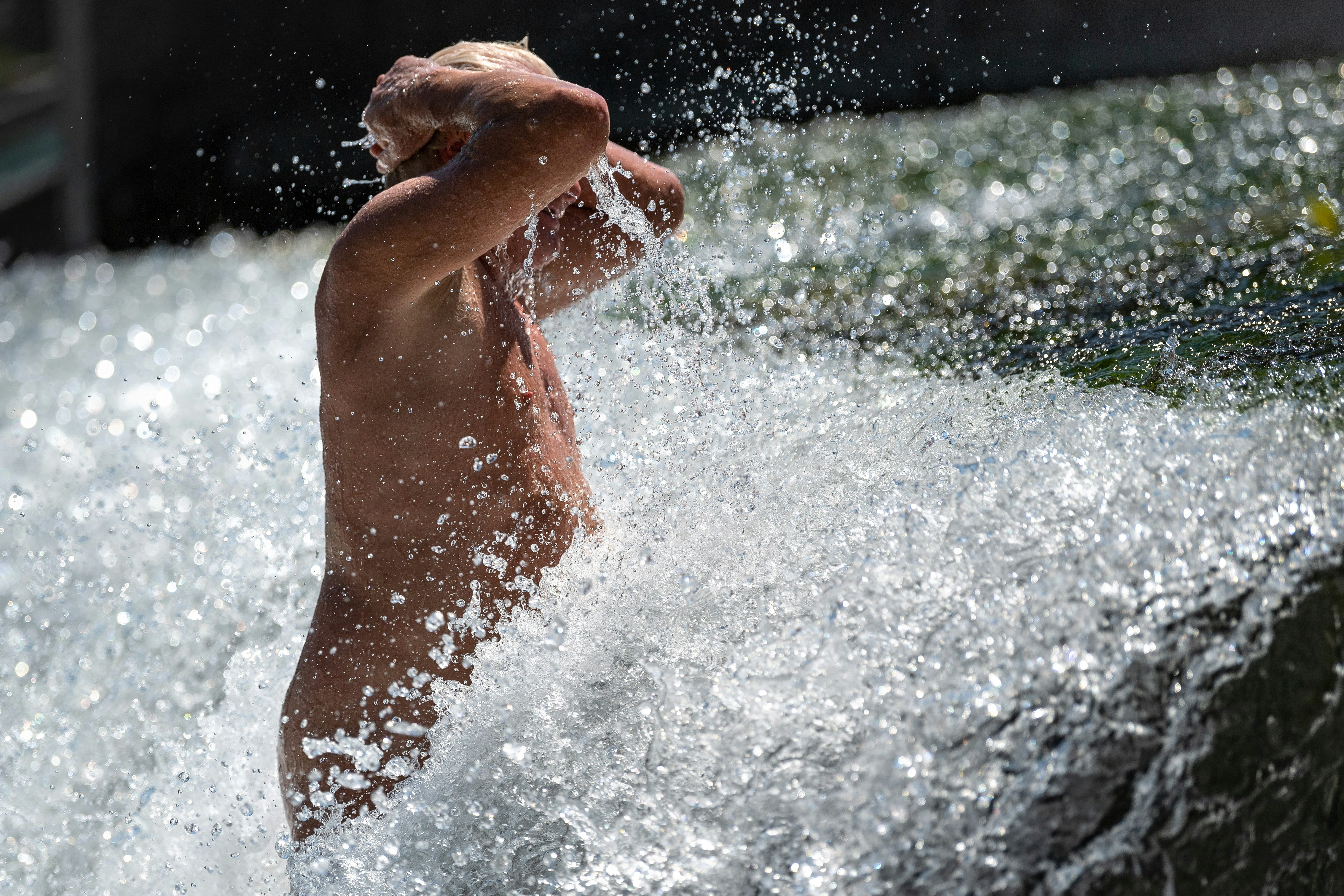An older nude man cools off in a huge rush of water 