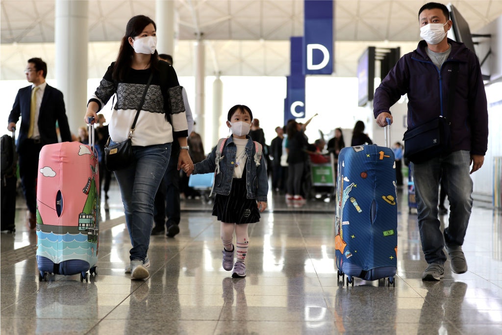 Travelers wearing face masks and pushing suitcases walk through the check-in hall at the Hong Kong International Airport in Hong Kong, China.