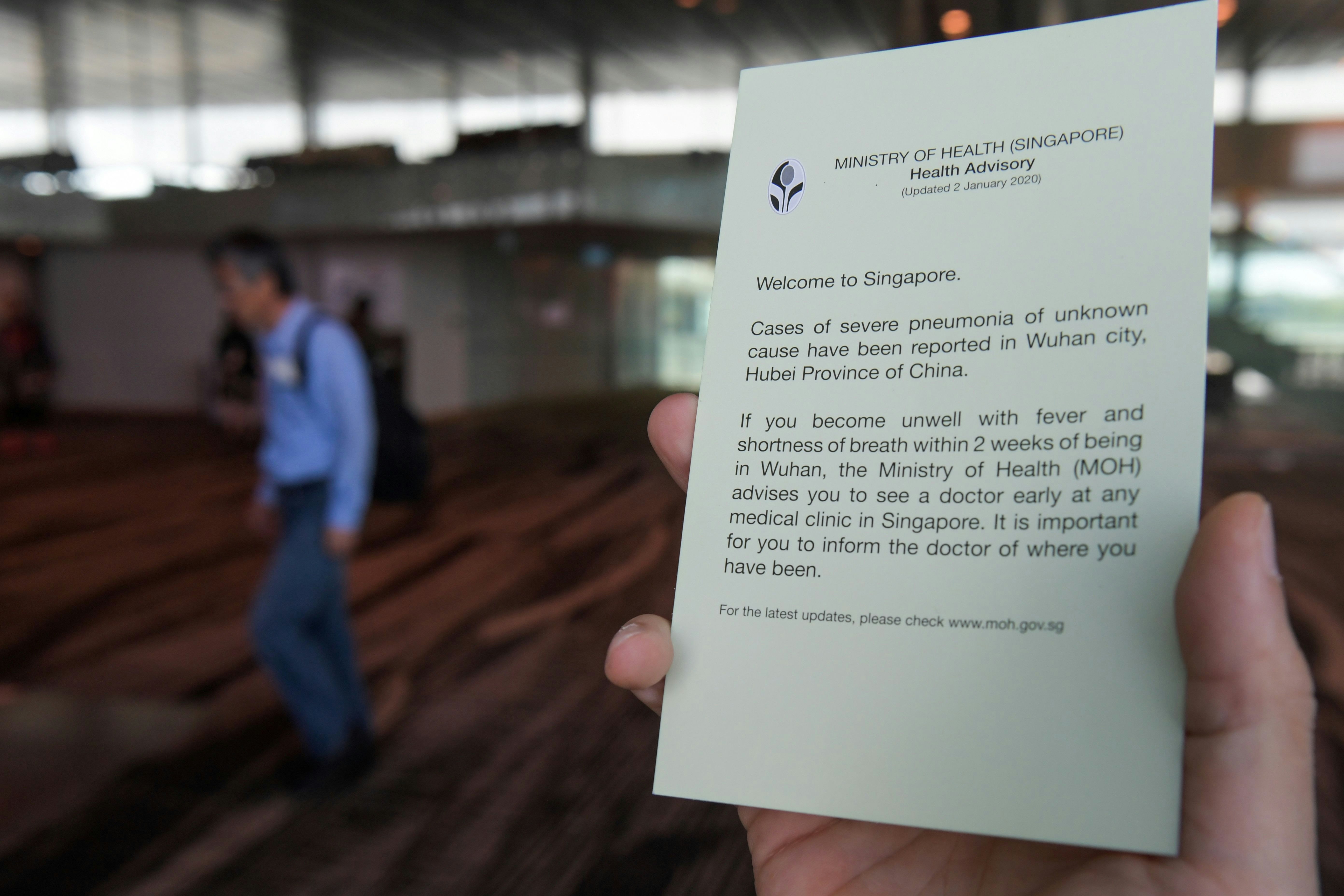 An airport staff holds health advisory cards for passengers at Changi International airport in Singapore.