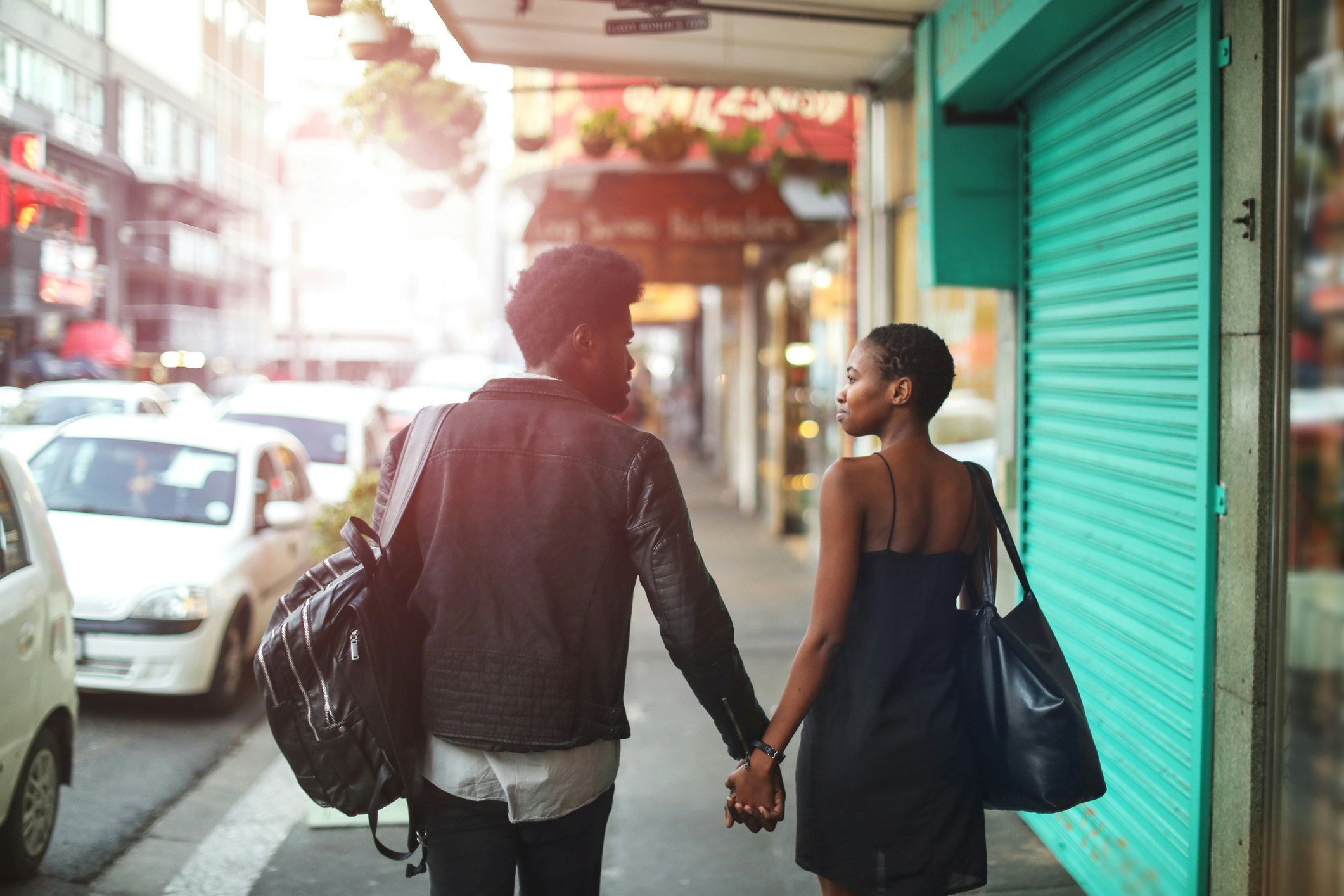 A couple hold hands walking on an urban sidewalk