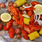 A pile of crawfish, potatoes, corn on the cob with a side of onions and a lemon wedge lay on old newspaper.