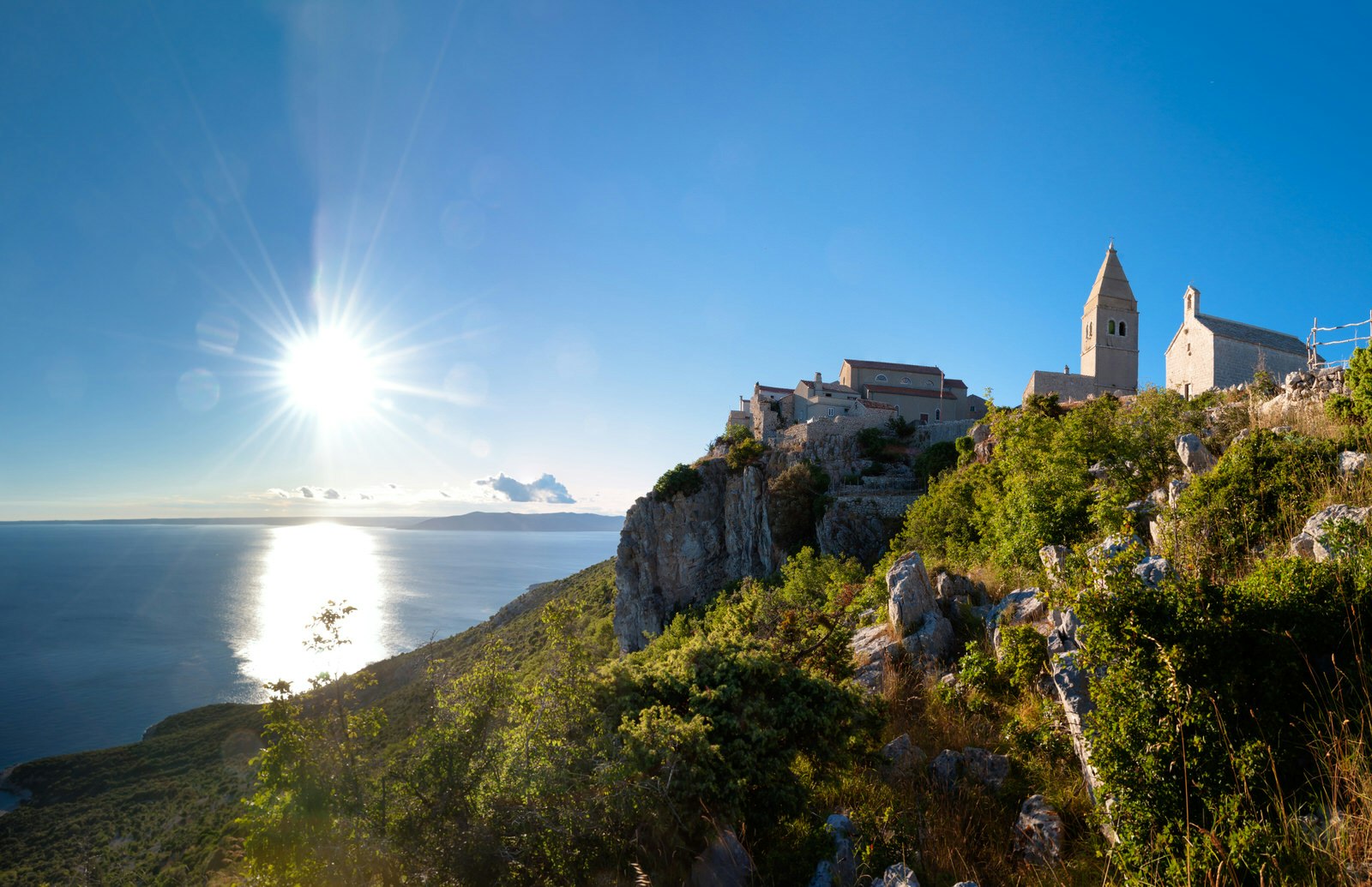 The sun shining low in the sky over the ancient town of Lubenice on the cliff side of Cres Island