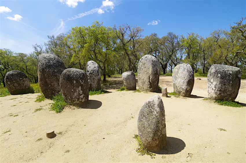 Cromlech Almendres - spring equinox.jpg A collection of stone circles are placed in a semi circle on a sandy clearing near a forest in Portugal.