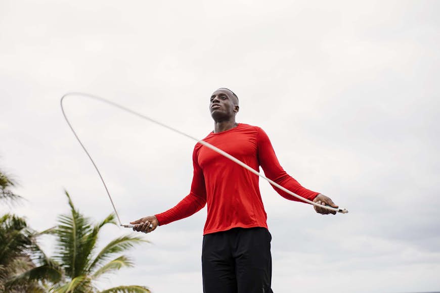 En man i en röd tee som hoppar rep, med palmer i bakgrunden