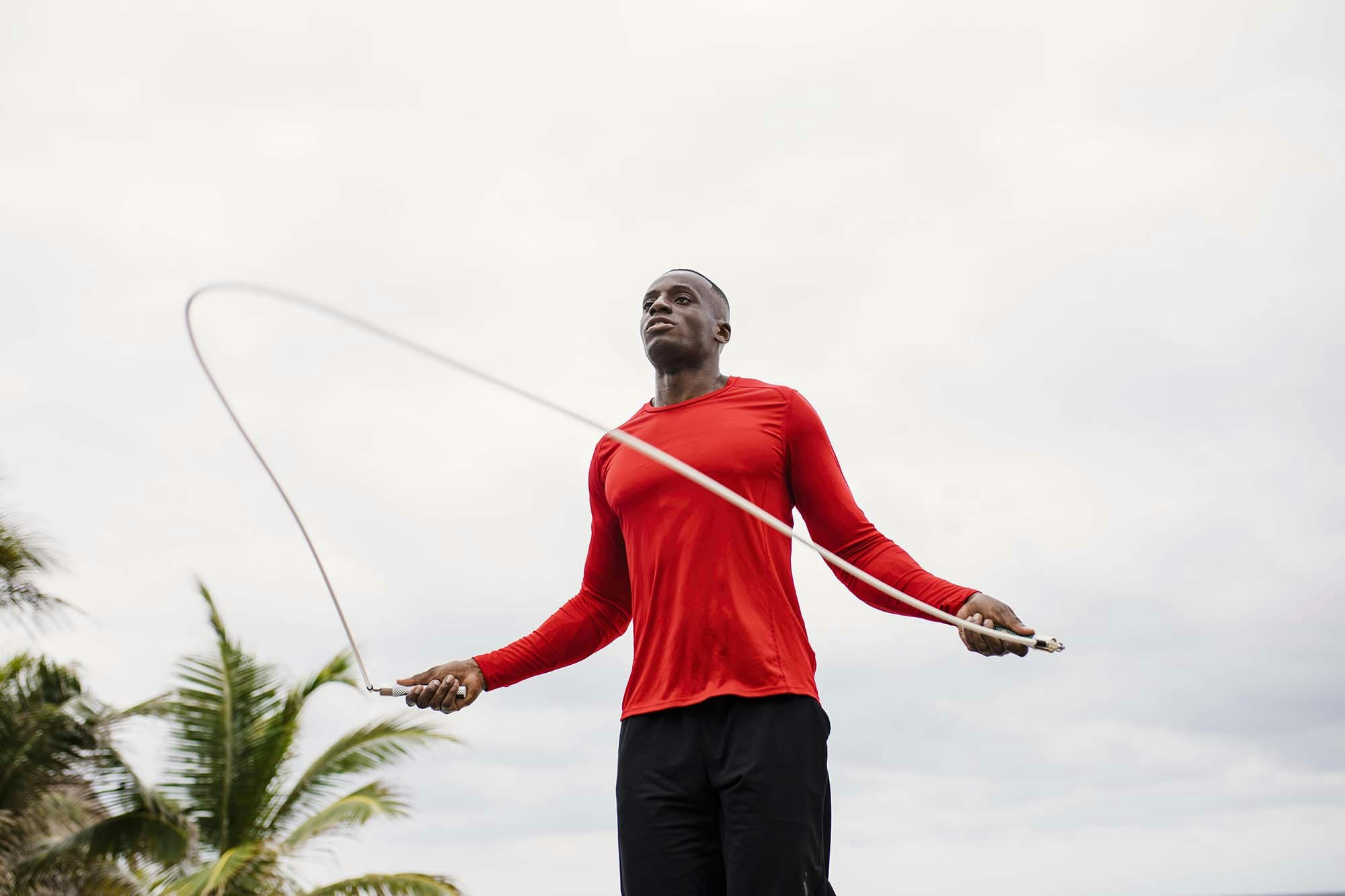 A man in a red tee jumping rope, with palm trees in the background