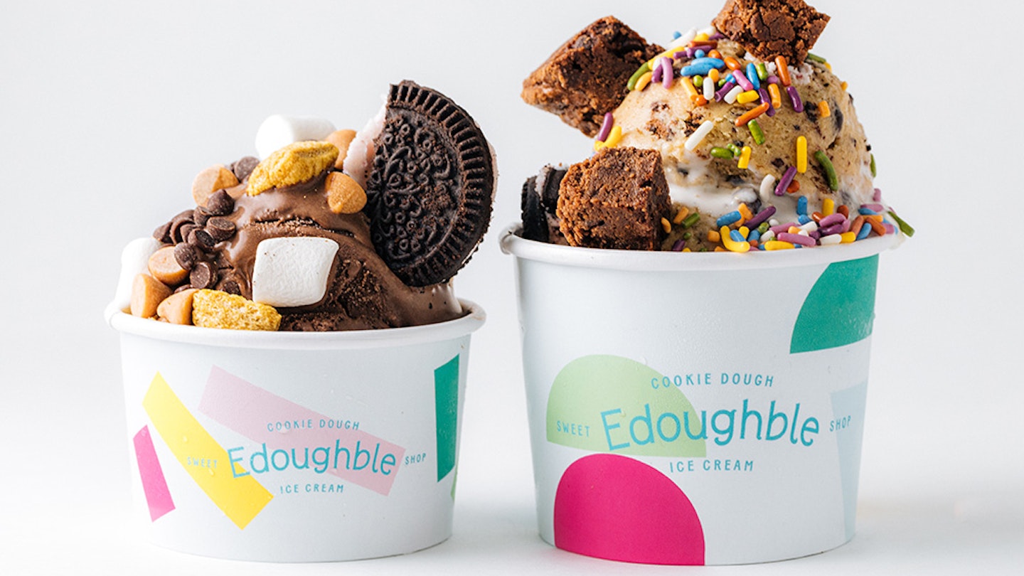 Two Edoughble cups holding cookie dough with cookies, marshmallows, sprinkles, and other mix-ins