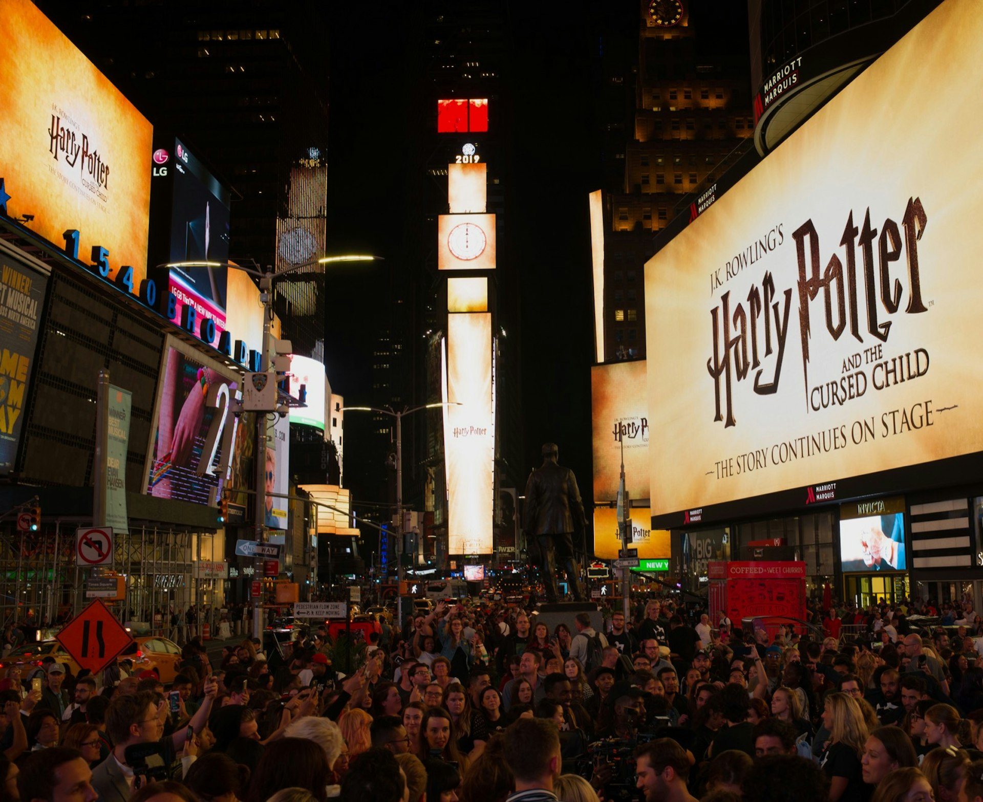 A brightly lit yellow marquee reads Harry Potter and the Cursed Child in front of a crowd of people at night
