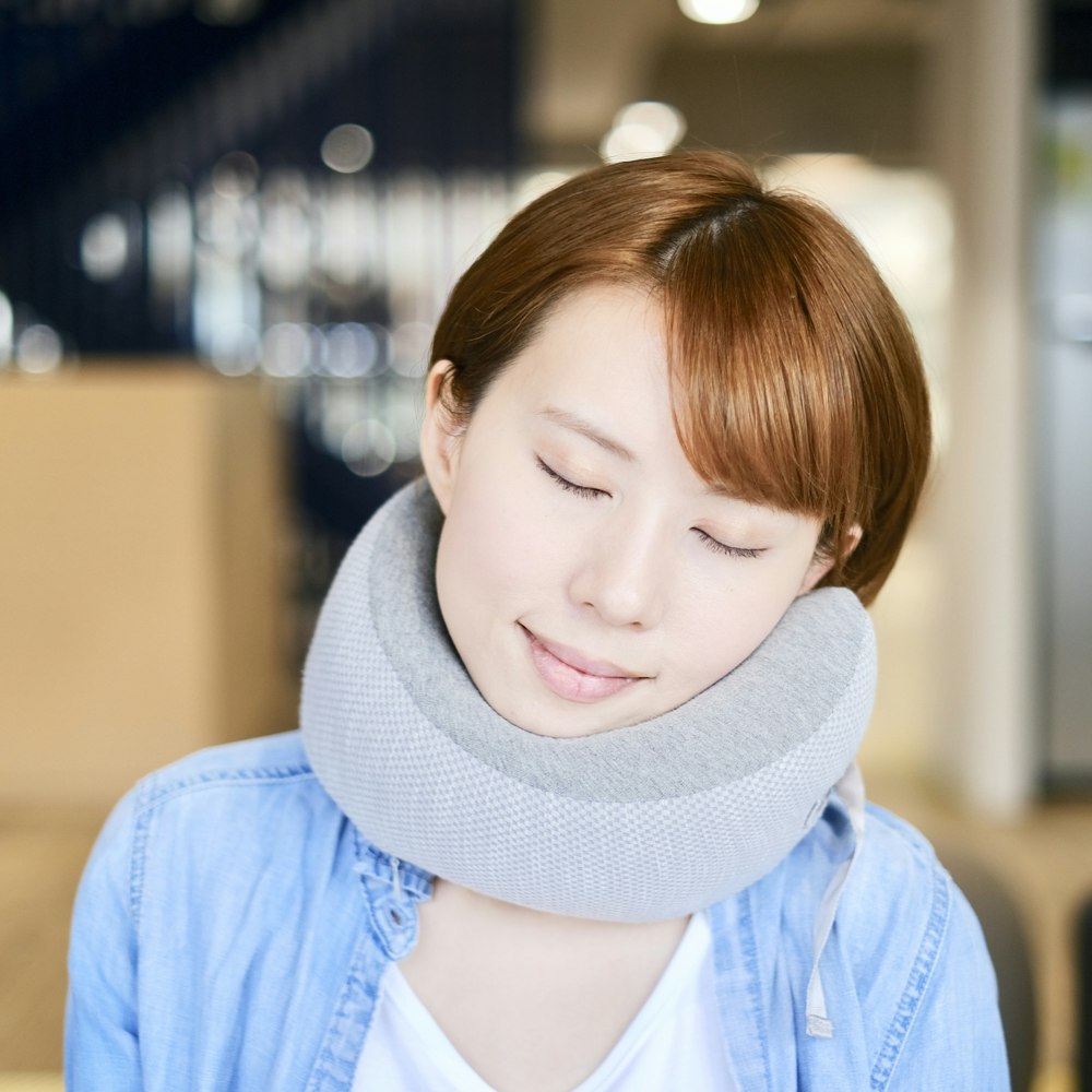 A woman sleeping with her head tilted, using Cushion Lab's grey Ergonomic Travel Pillow 