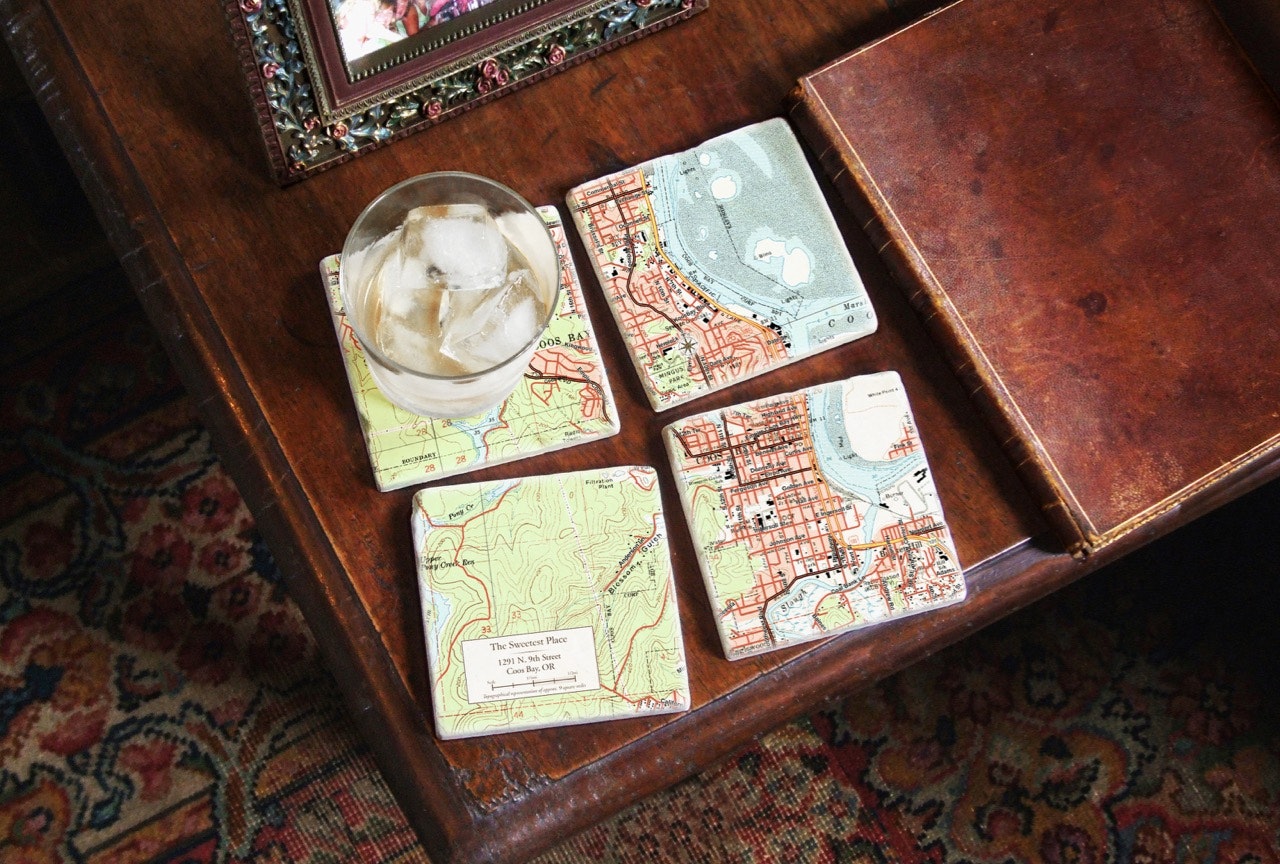 A table with four map-printed coasters in a grid, one holding an ice-filled beverage