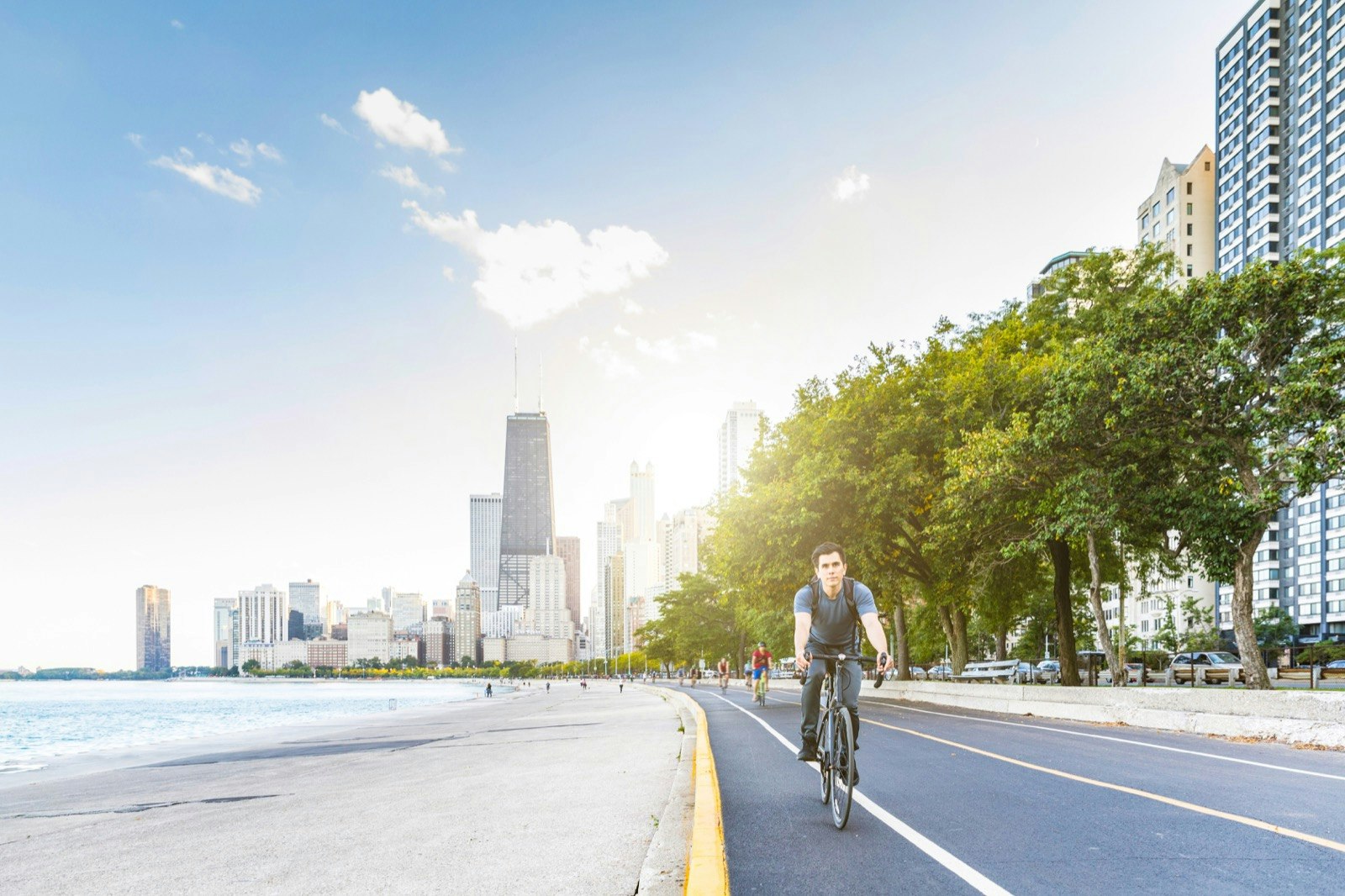 A man rides his bike along the waterfront with the city skyline in the background