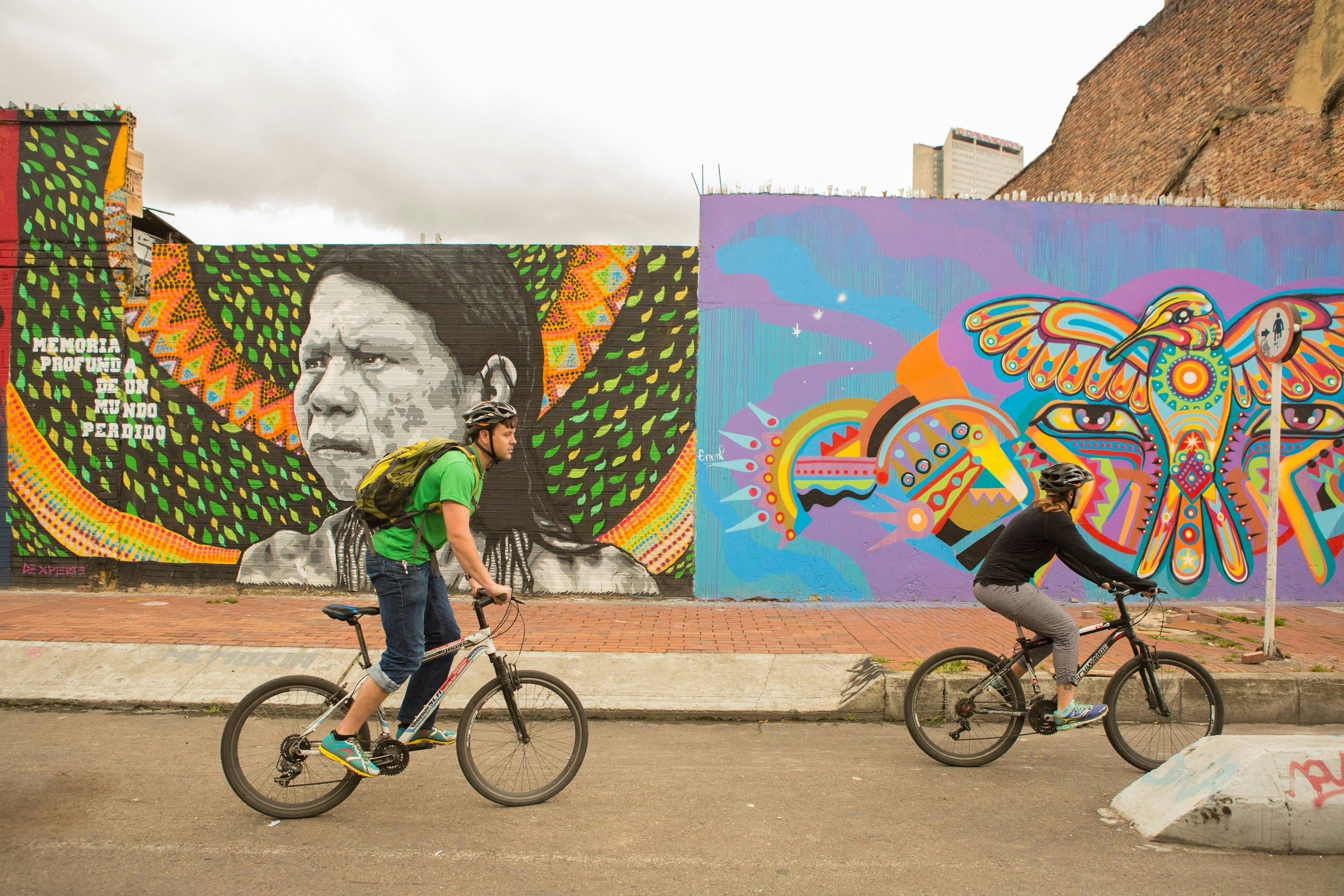 Two cyclists on mountain bikes ride past a long mural that runs the length of a street