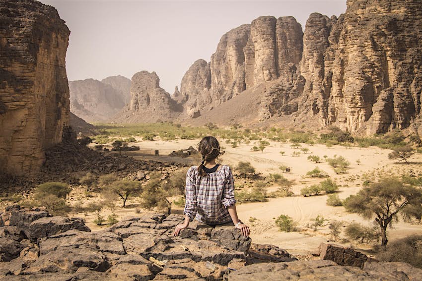 DJANET, ALGERIA - Shutterstock RF.jpg Young woman sitting on the stones and looking at Tuareg tribe settlement in Sahara desert