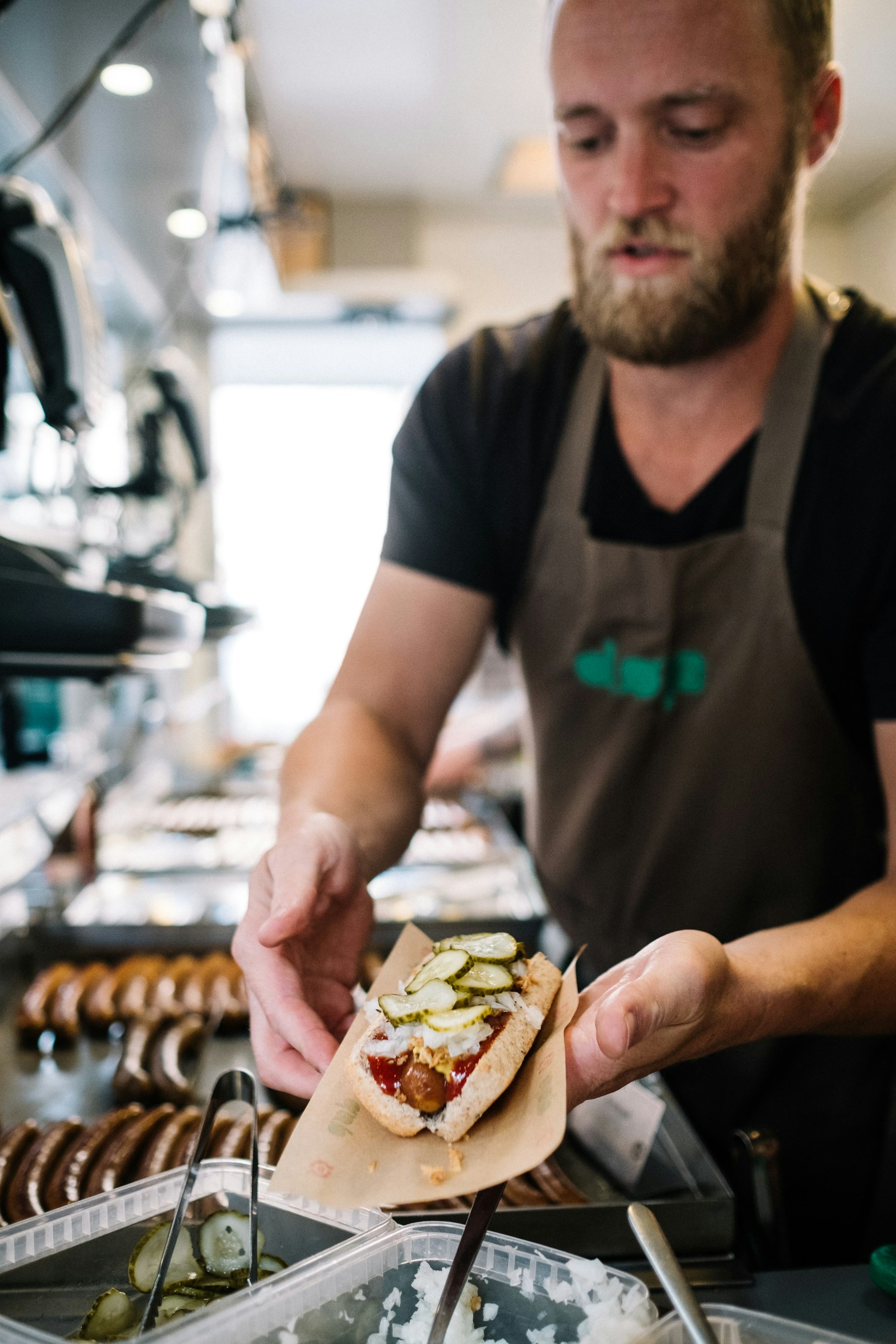 A man prepares toppings for a Danish-style hot dog that he is holding.