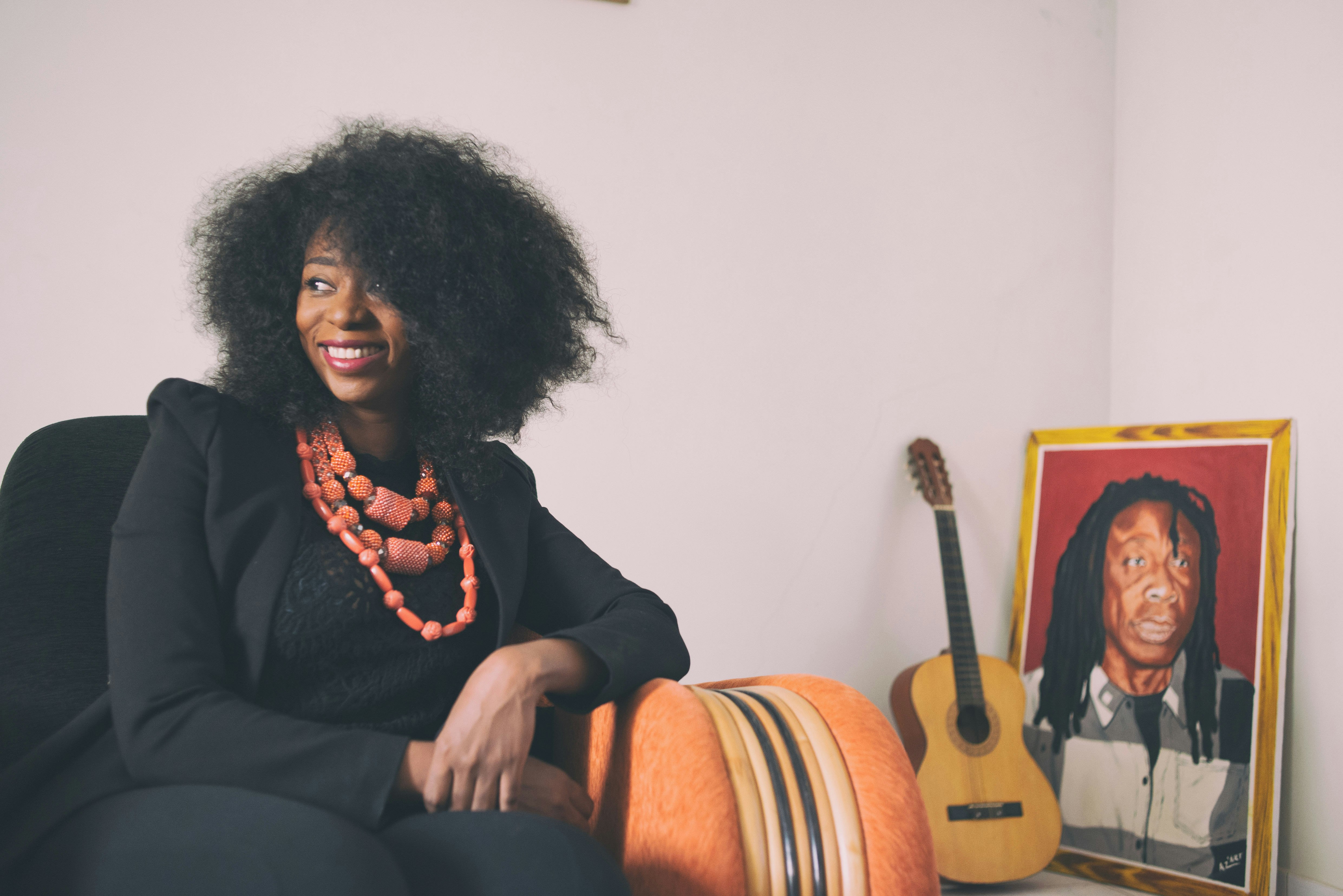 Adiouza, dressed all in black with three large coral-coloured necklaces, sits in an arm chair; a portrait of her father, the musician Ousmane. Diallo, alias Ouza, sits on a table to her side.