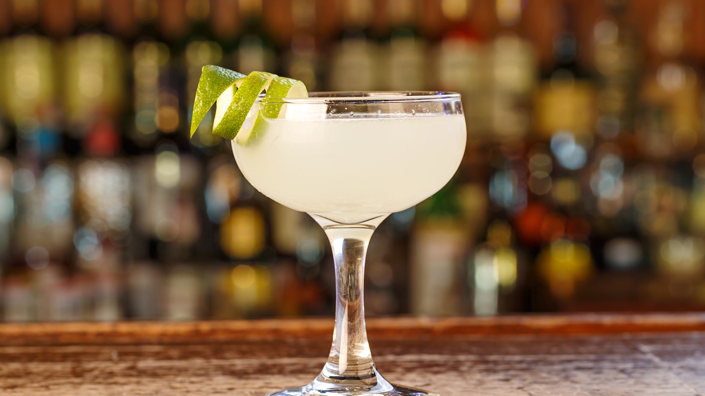 A spiral cut lime wedge hangs off the rim of a chilled glass of a Cuban daiquiri 
