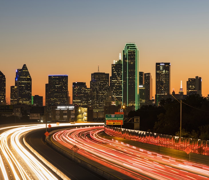 Buildings making up the downtown skyline shine bright in the night sky. Below is a blur of headlights on the highway