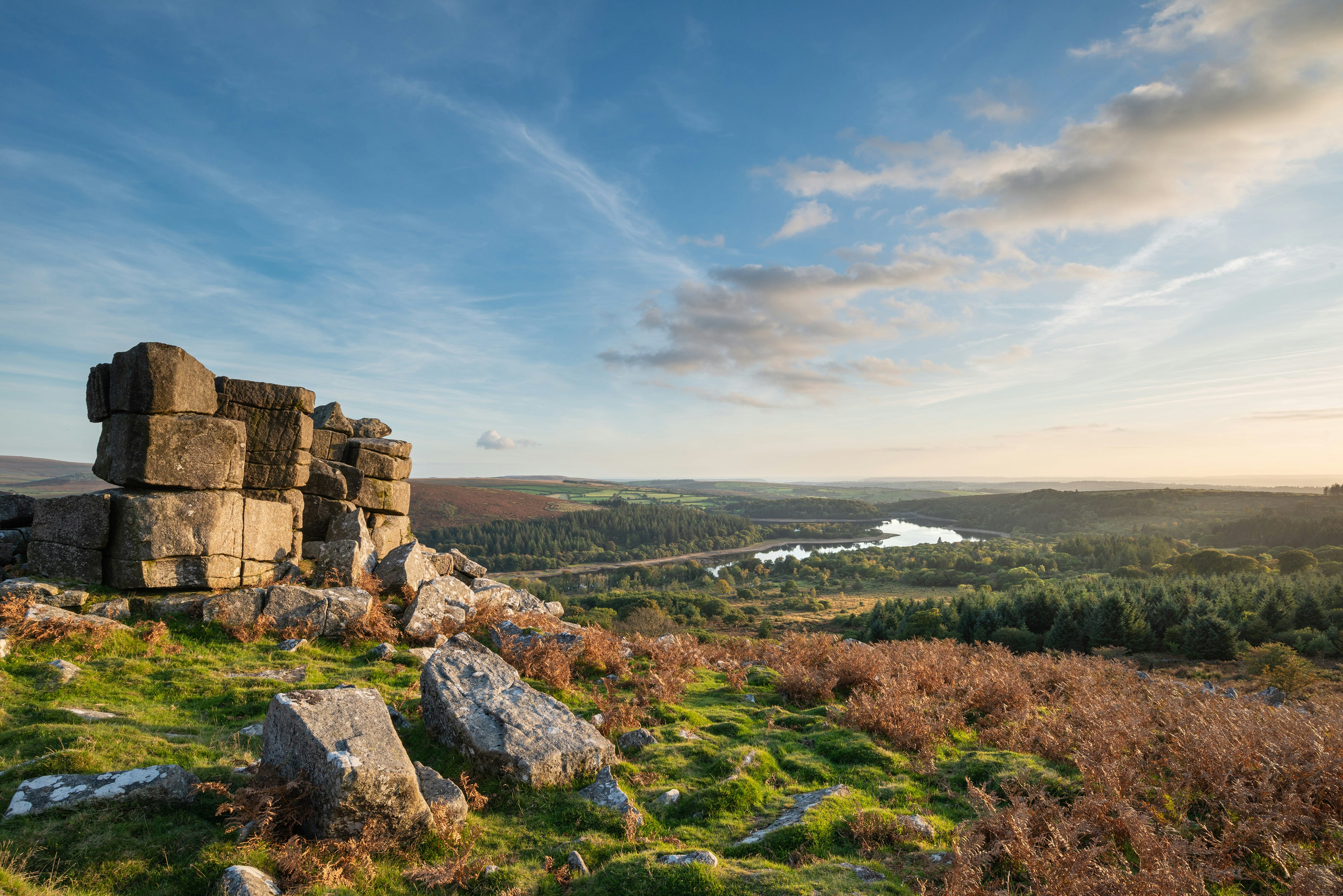 A scenic view of Dartmoor National Park in England. The park is filled with forests and has a river running through it.