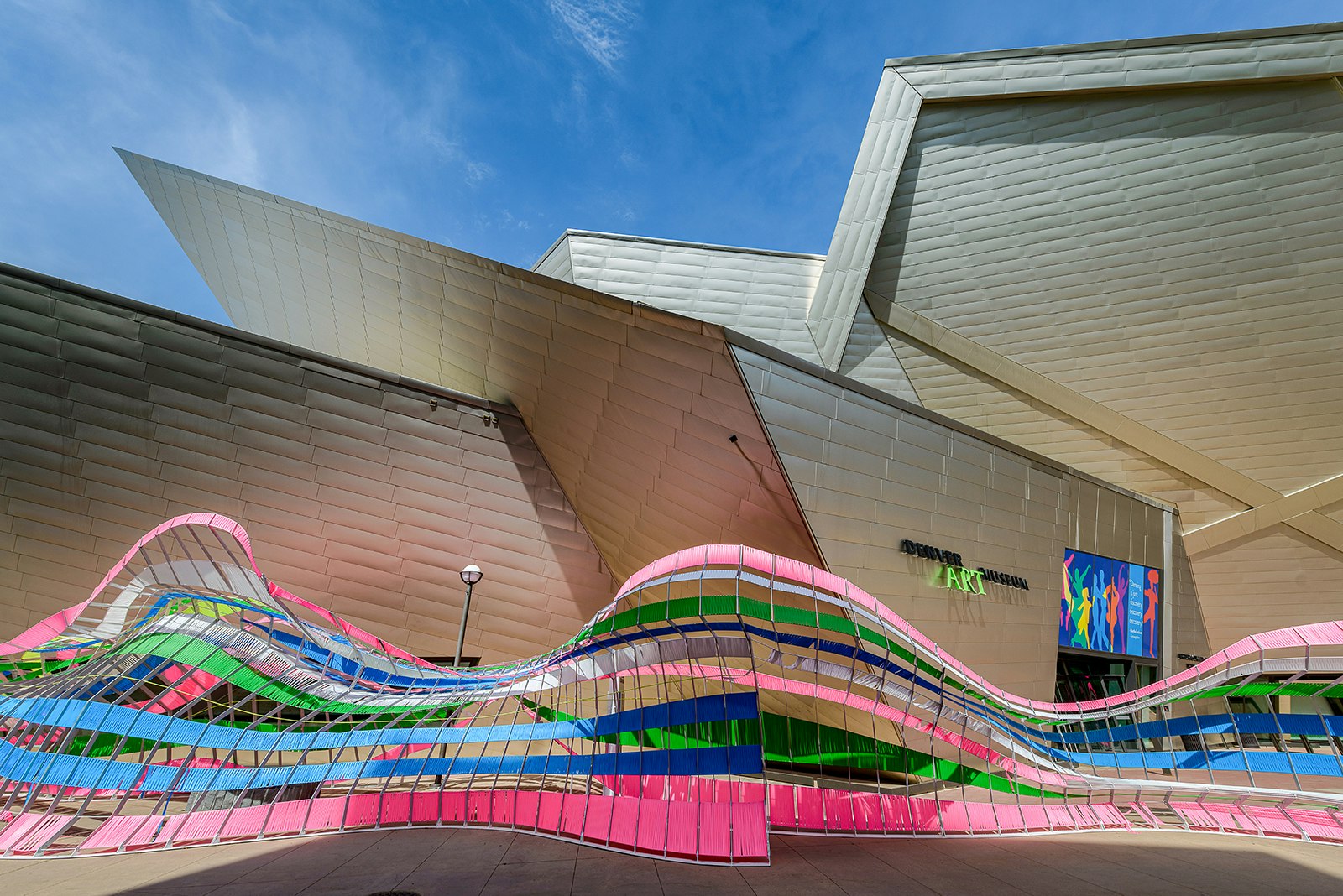 A wavy, multicolored art installation sits in front of the Denver Art Museum, which is characterized by its metal, geometric architecture. Denver, Colorado.