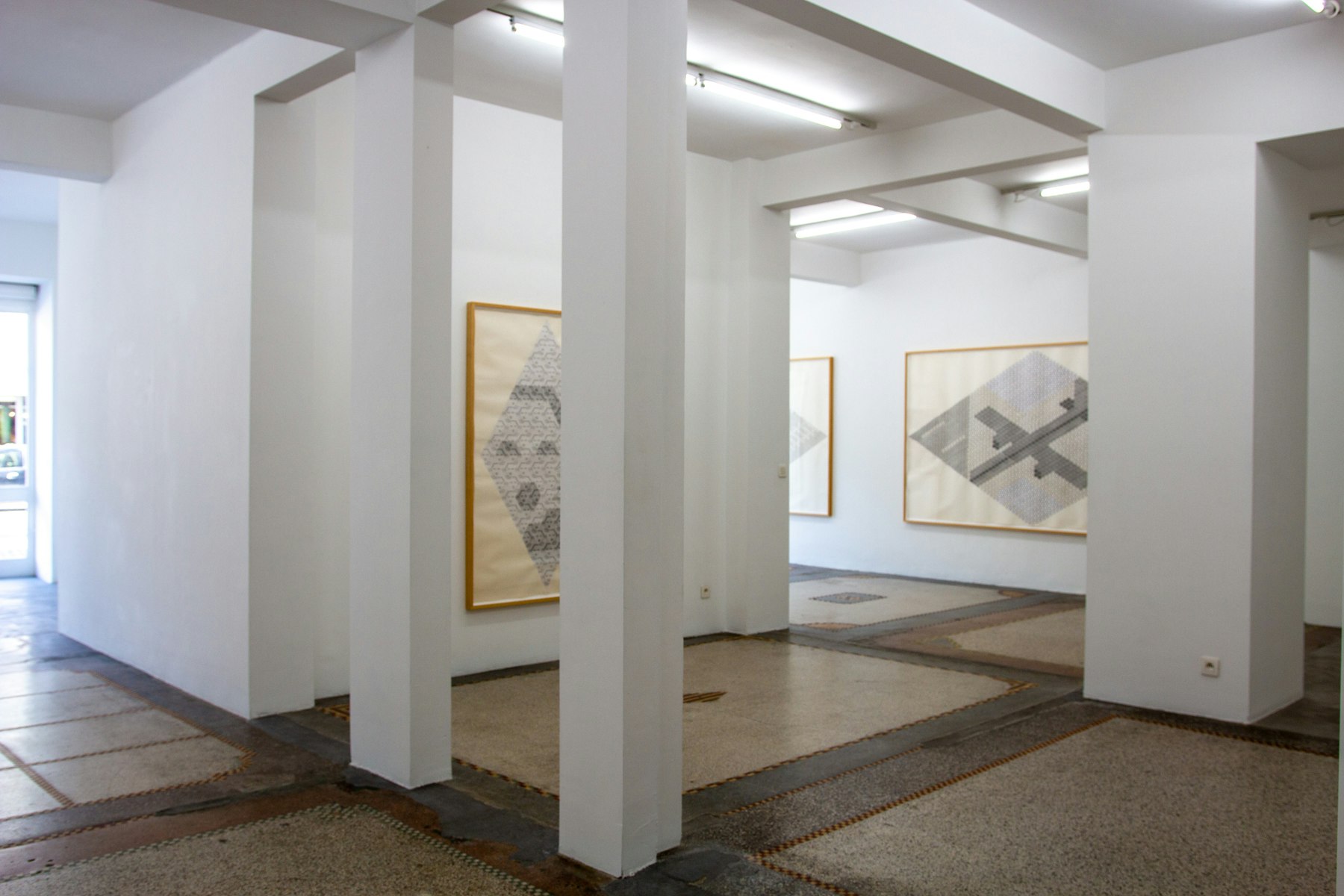 A gallery interior with white walls and columns, and contemporary art on the walls; there is a stone floor with large paving slabs in grey and cream.