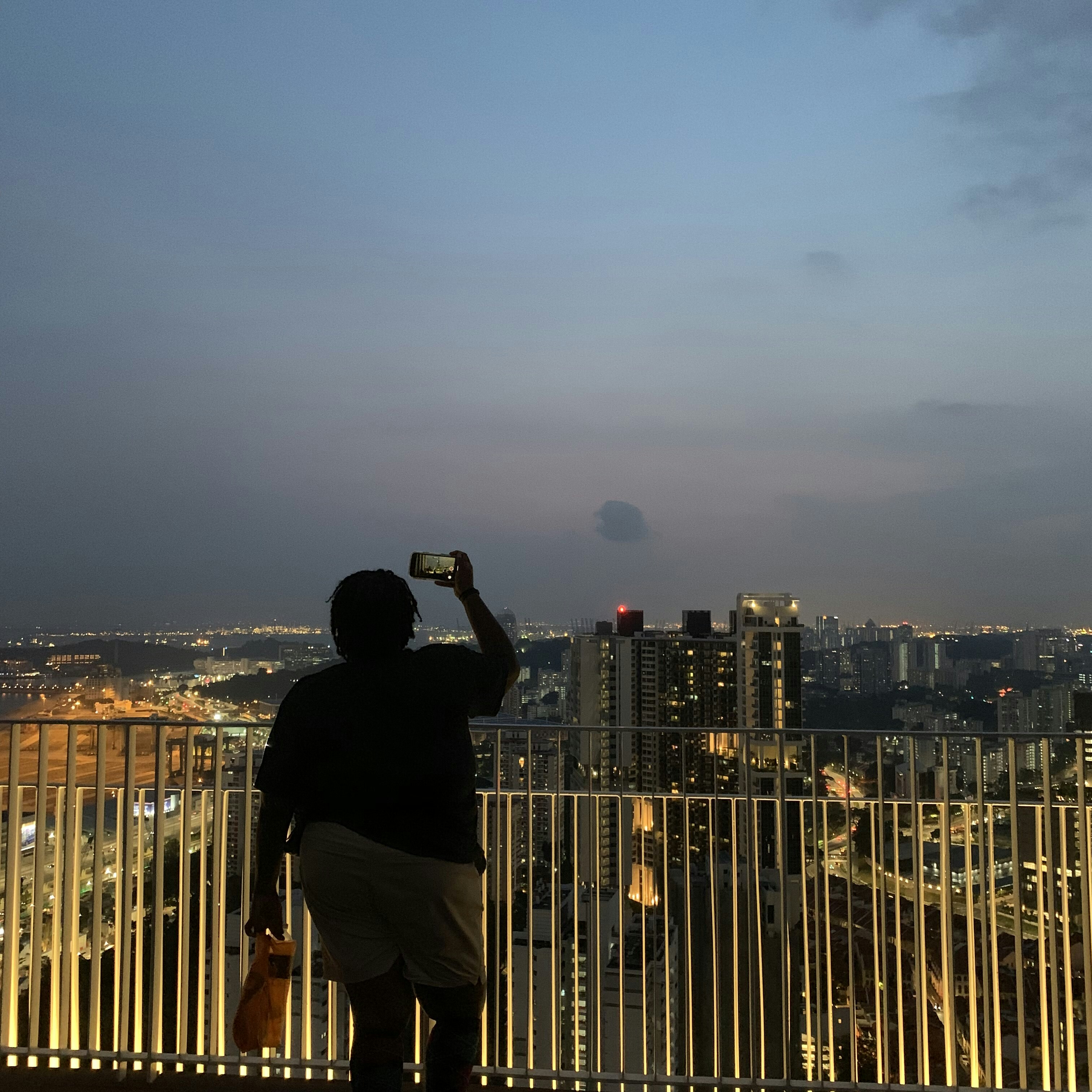 A woman takes a photo of the Singapore skyline on the top of the Singapore building in the early evening