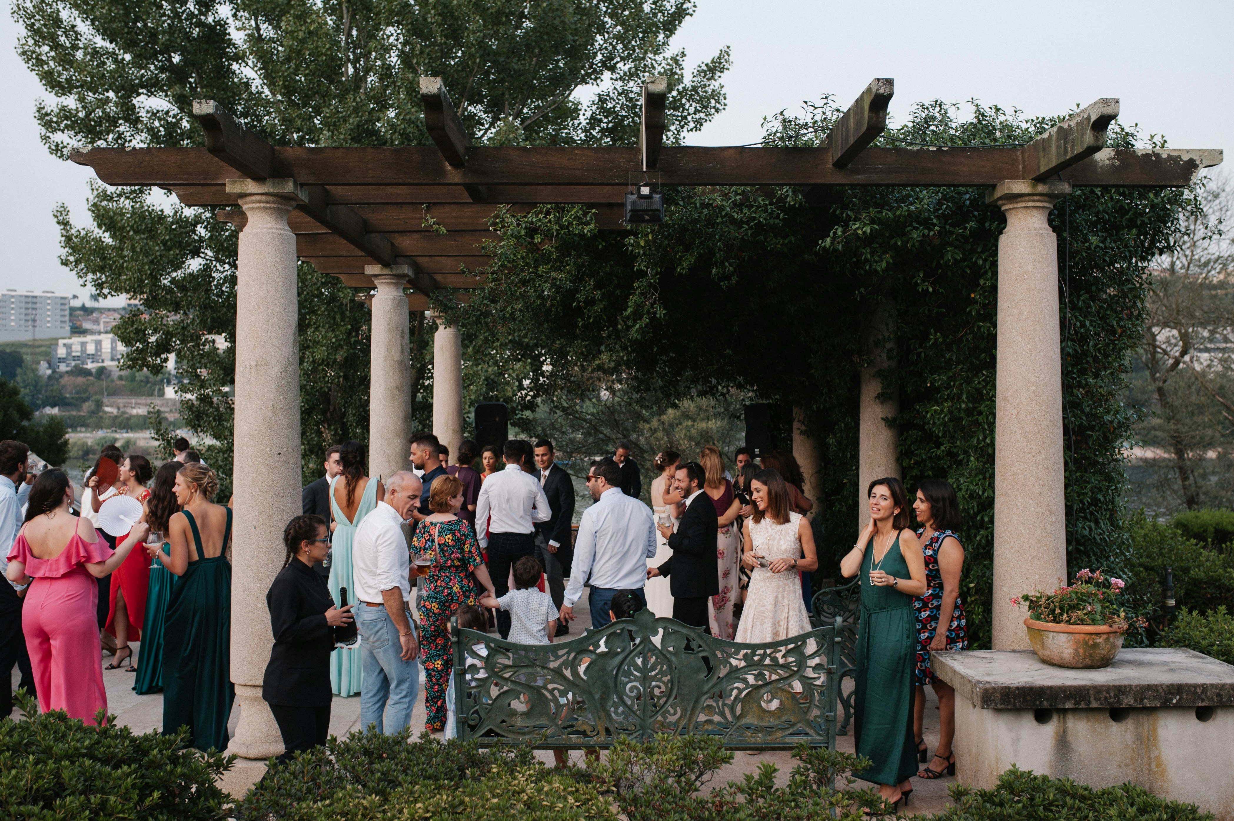 A group of wedding guests are standing together outside under a decorated gazebo.