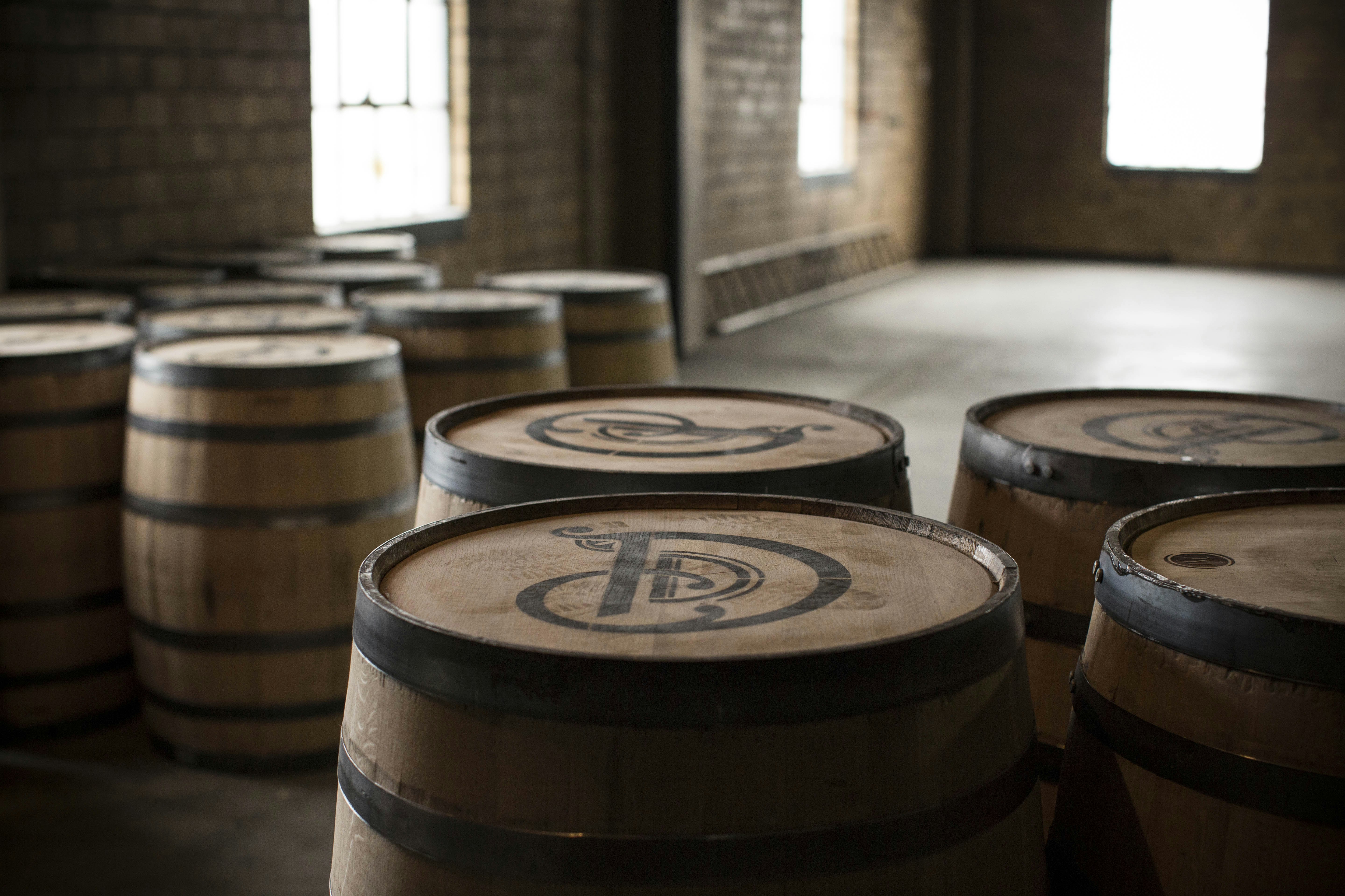 A row of wooden bourbon barrels sit in a large open warehouse; Unusual distilleries