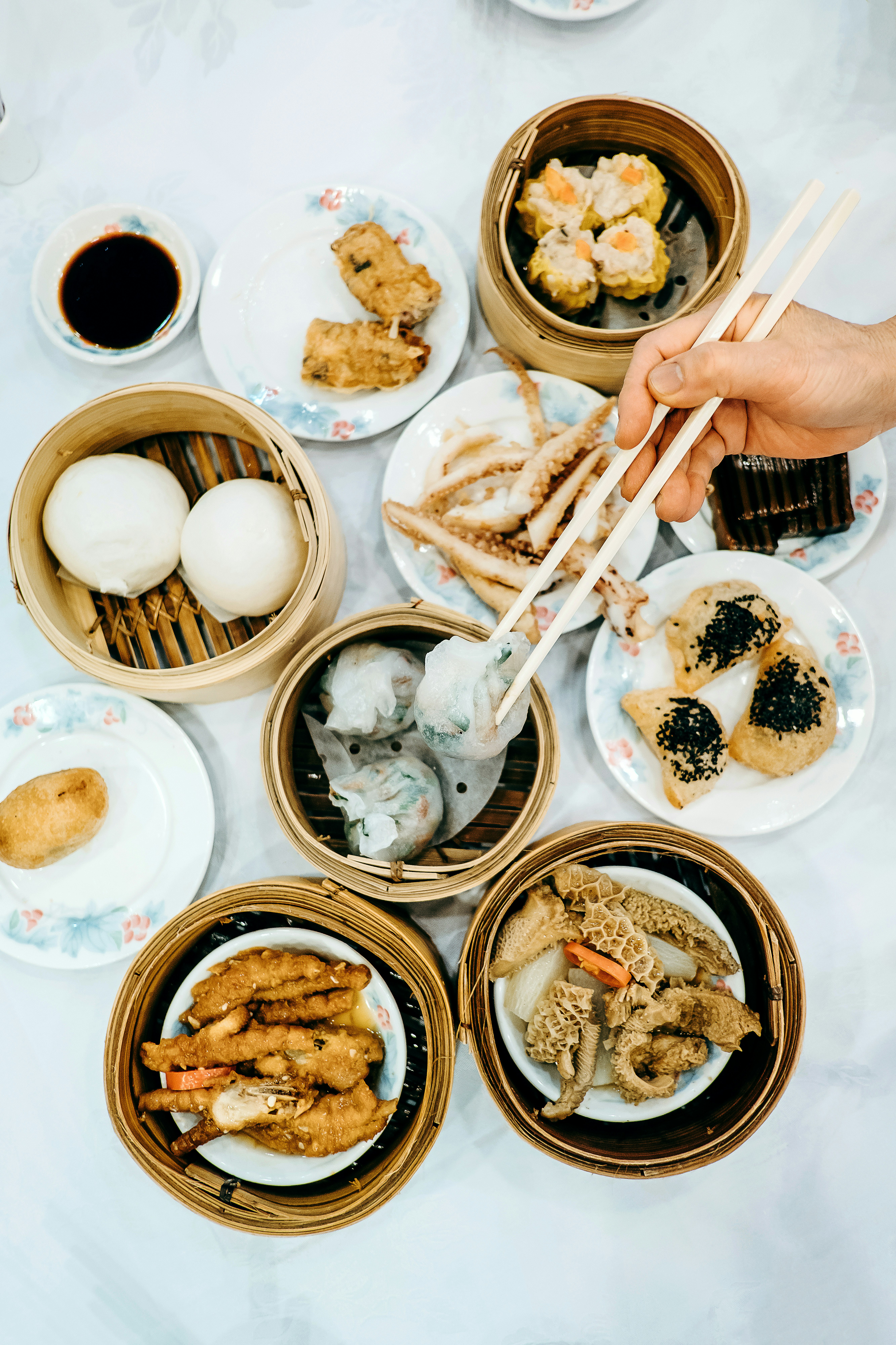 A variety of traditional dim sum served at a Hong Kong restaurant with a hand holding chopsticks reaching over the food. 