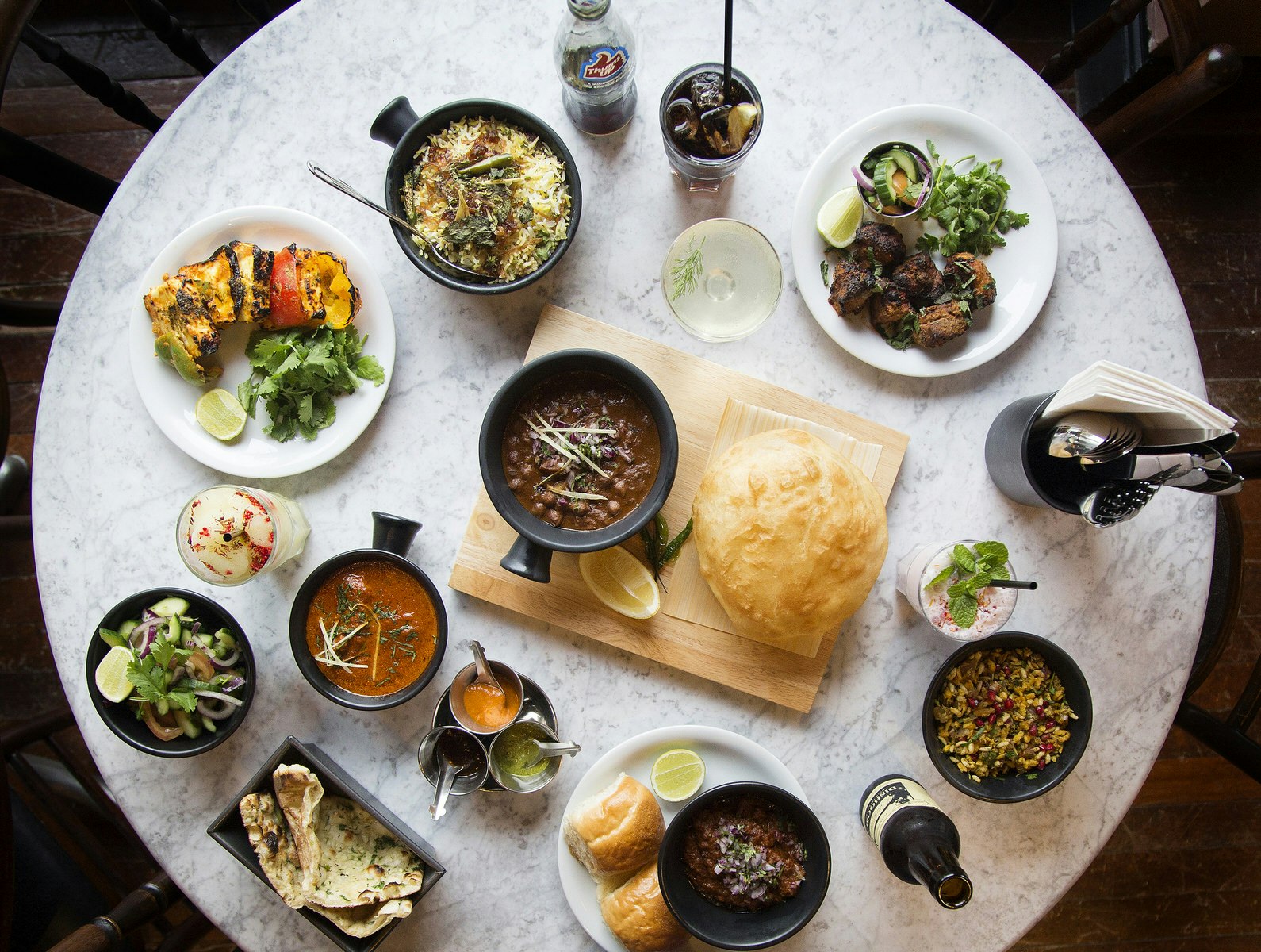 An aerial shot of a round, marble-topped table laden with several dishes and drink at Dishoom, Edinburgh. 