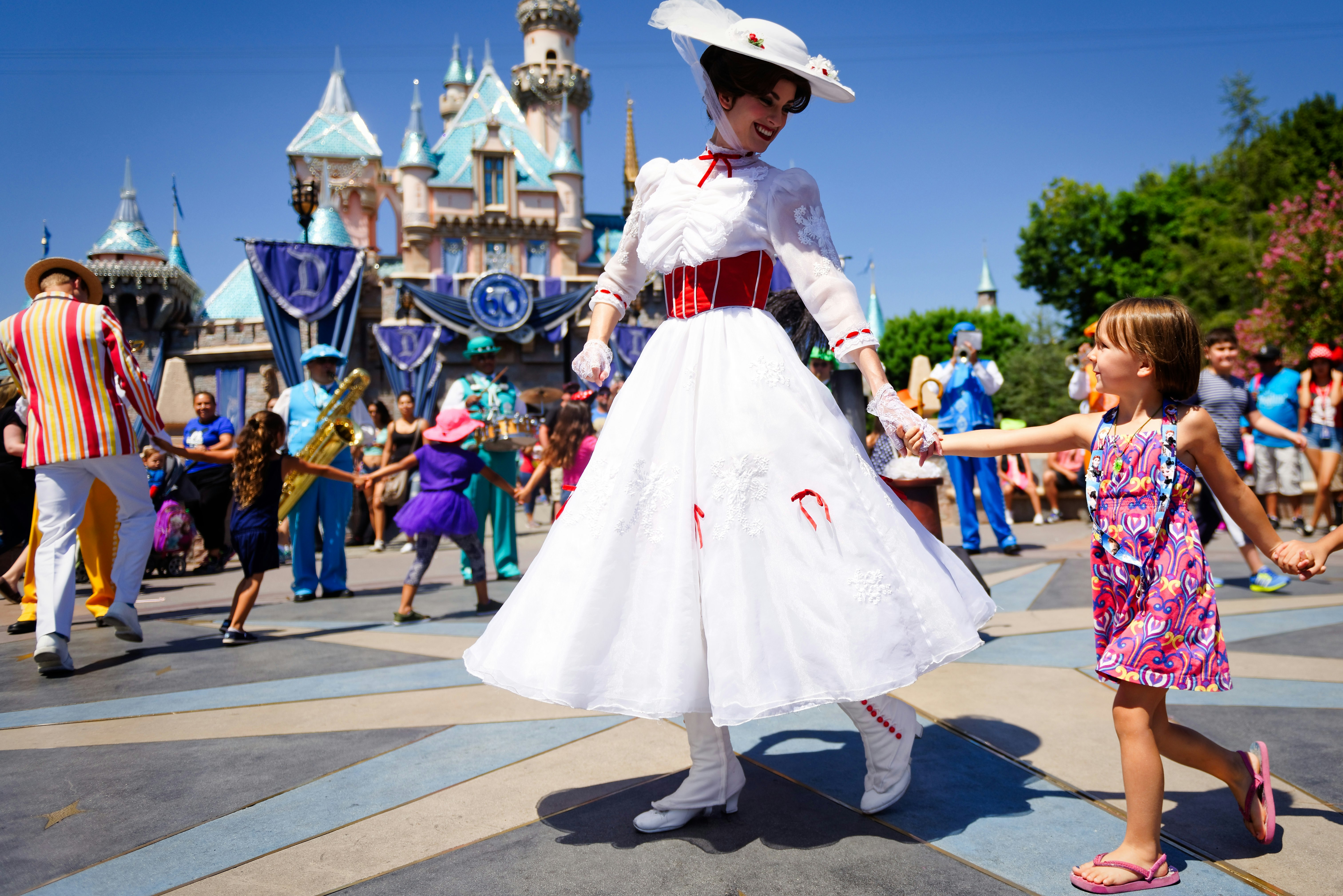 An actress dressed as Mary Poppins smiles at a young child as she leads a line of children in song and dance in front of Cinderella's castle during Disney's 60th Diamond Celebration at Disneyland California.